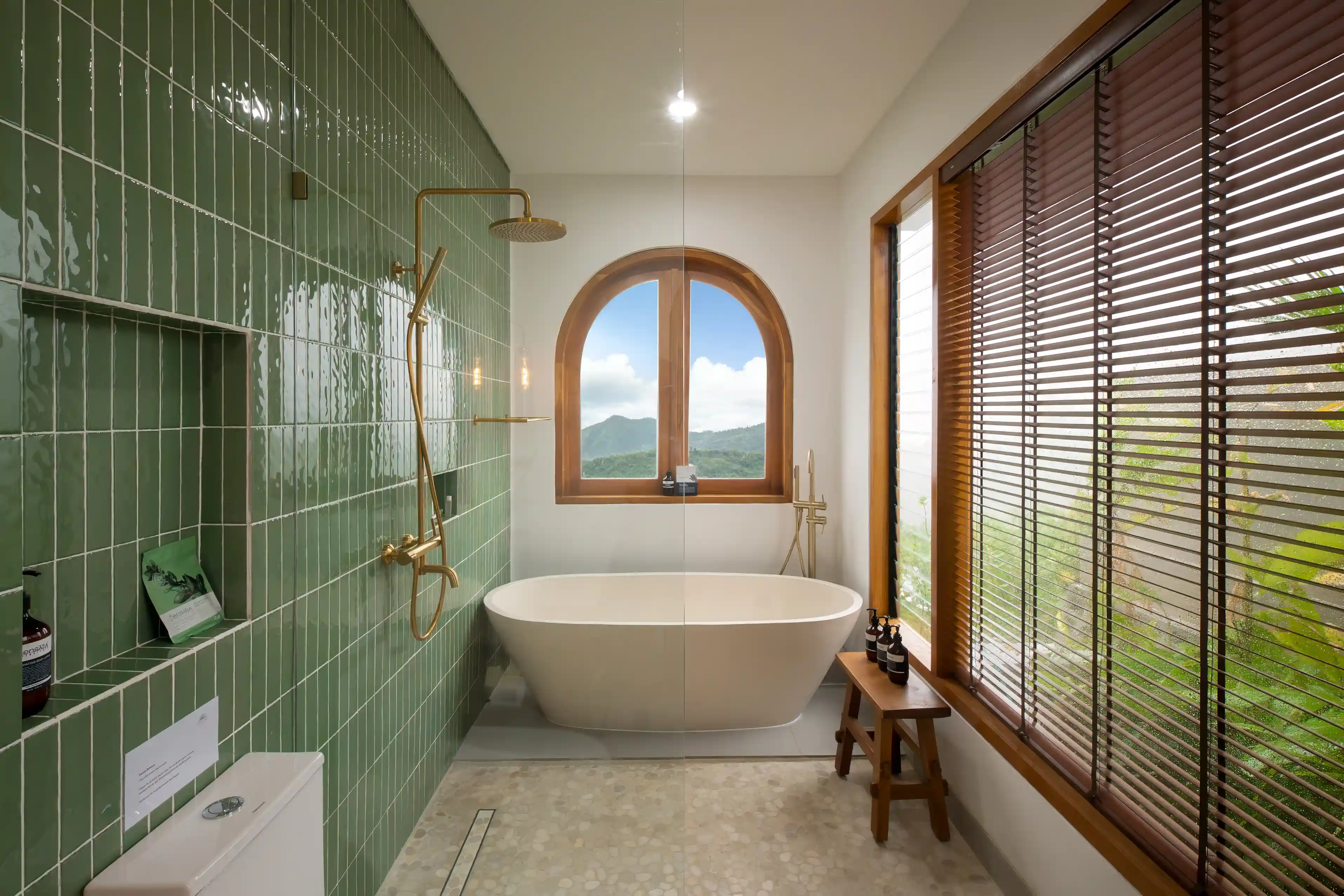 Salle de bain moderne équipée d'une baignoire îlot, douchette dorée et mur en carrelage vert brillant.