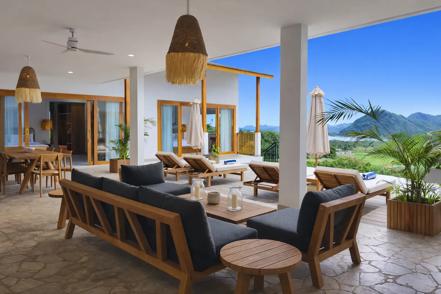 Terrasse couverte moderne avec canapés en bois, transats et vue imprenable sur la mer et les montagnes.