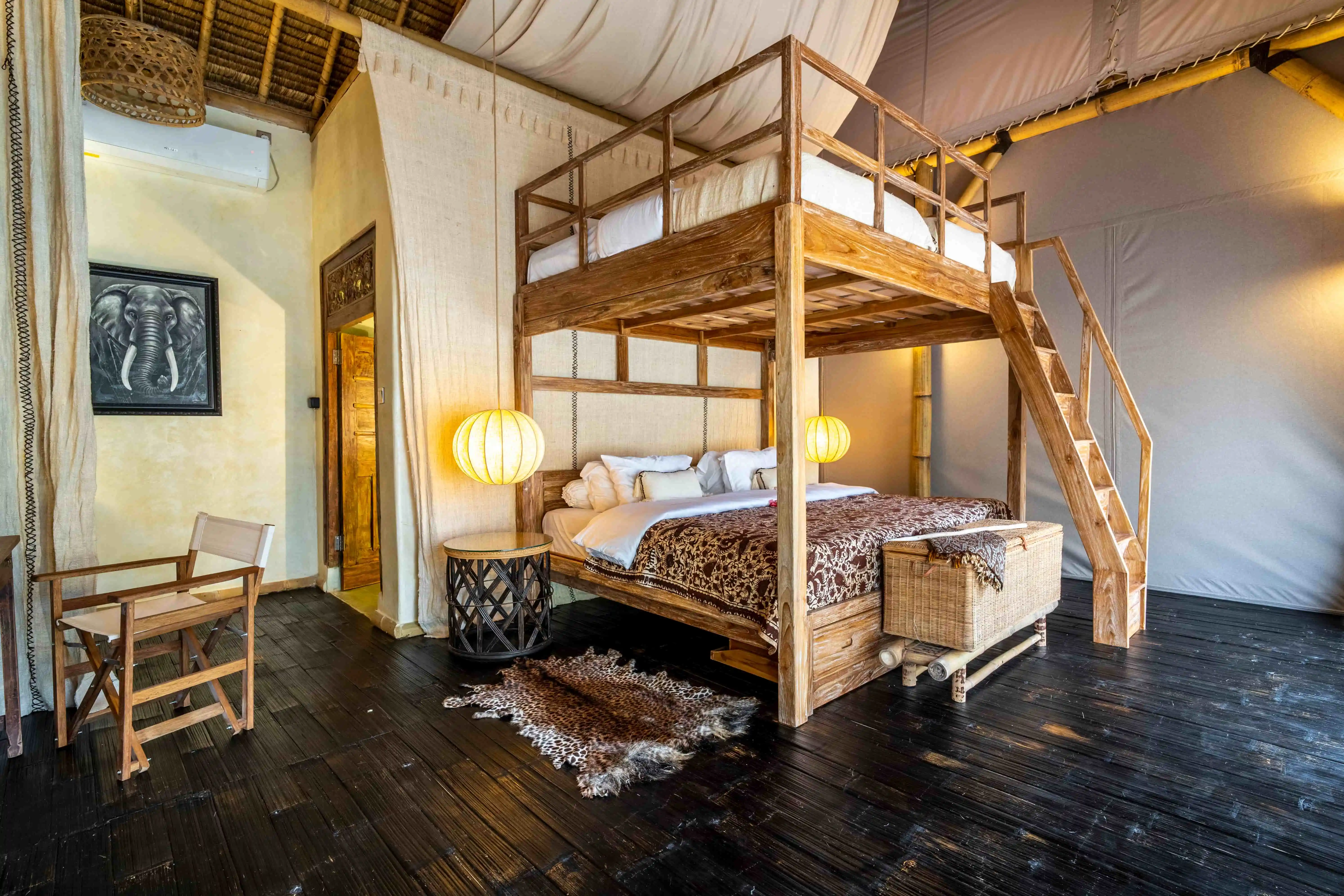 Luxury tropical villa bedroom with a wooden loft bed, king-size bed, natural wood furniture, and elegant safari-inspired interiors.