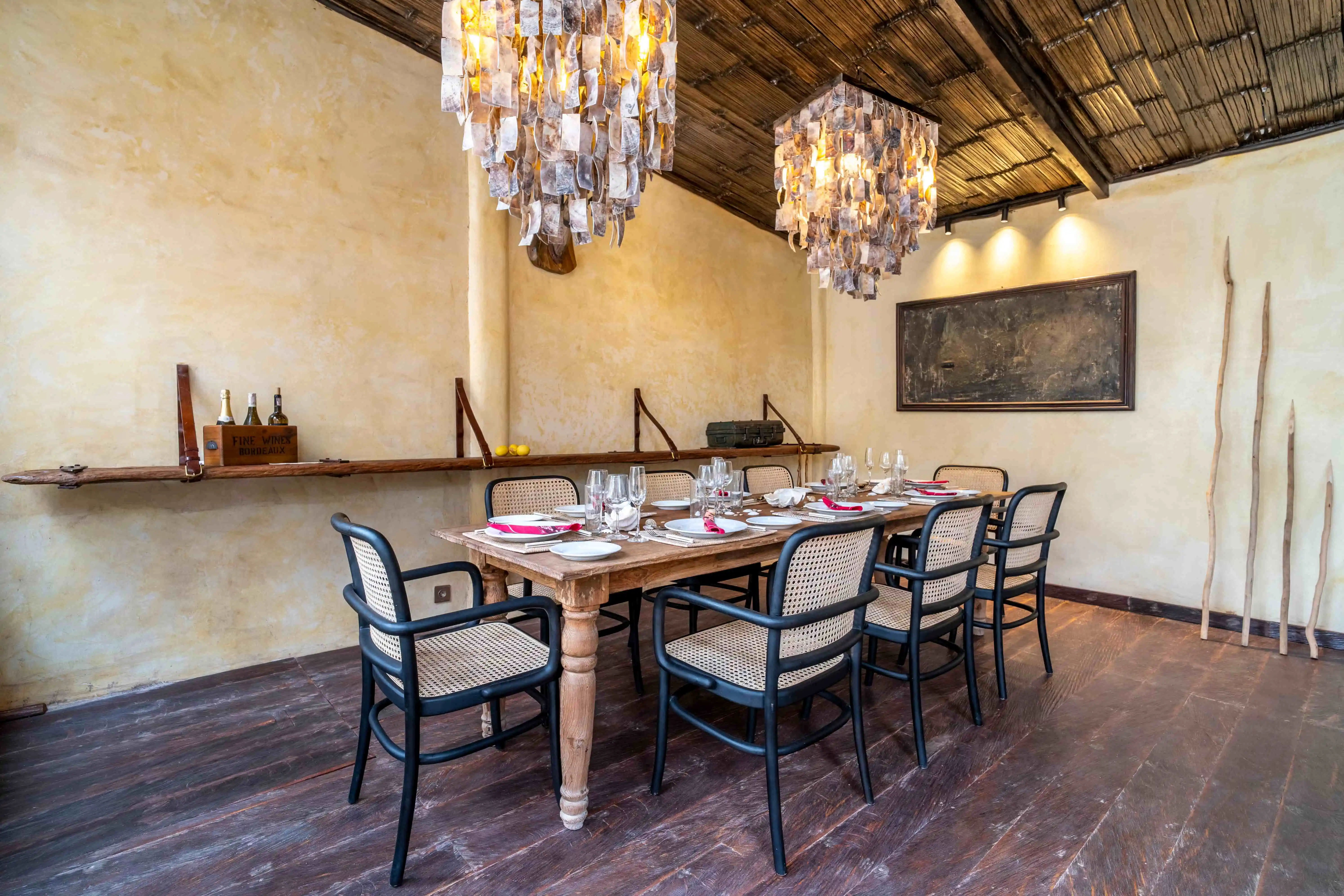 Spacious villa dining room featuring a solid wood table, woven chairs, statement chandeliers, and warm tropical design.