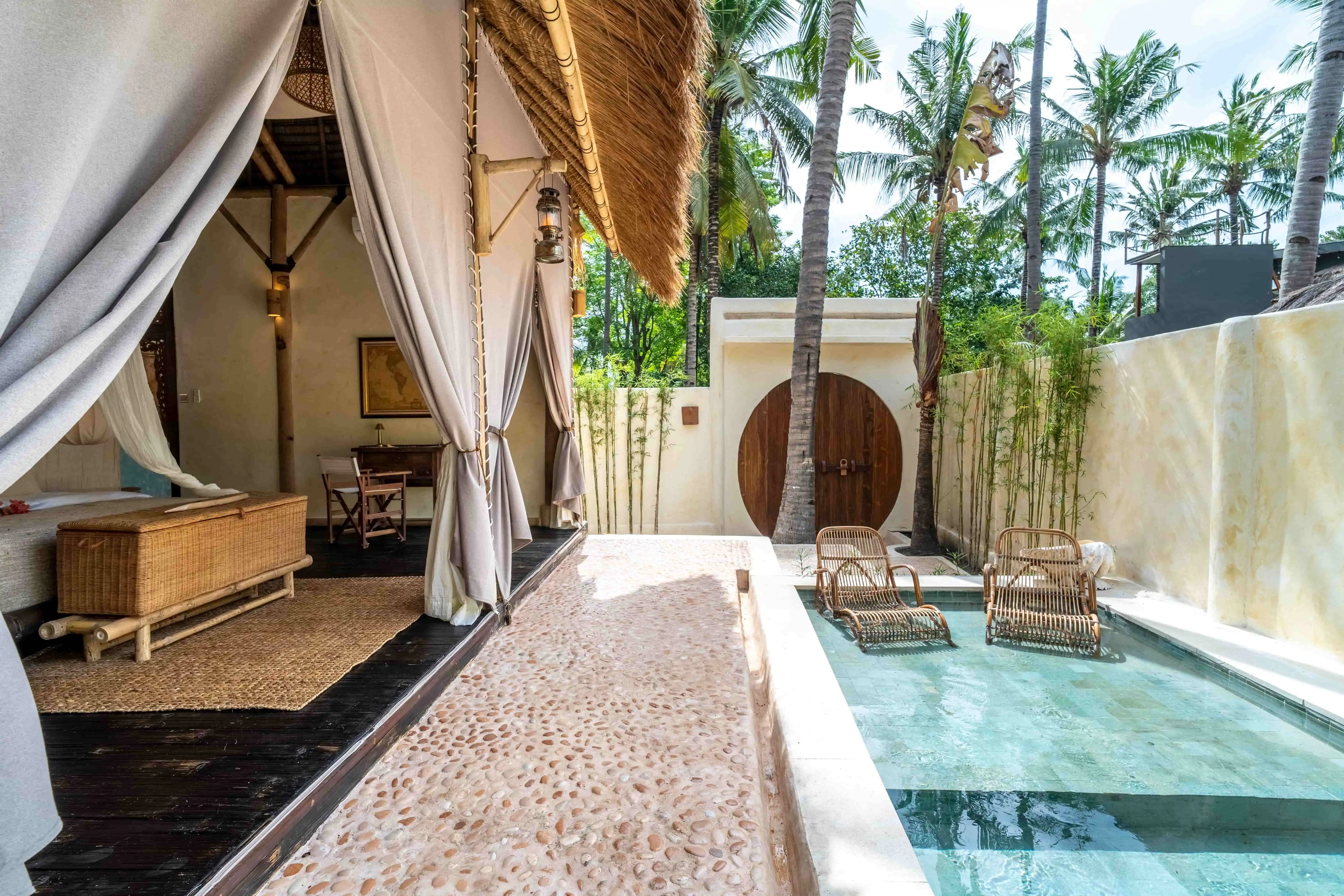 Private plunge pool with in-water lounge chairs beside an open-air luxury villa surrounded by tropical palm trees.