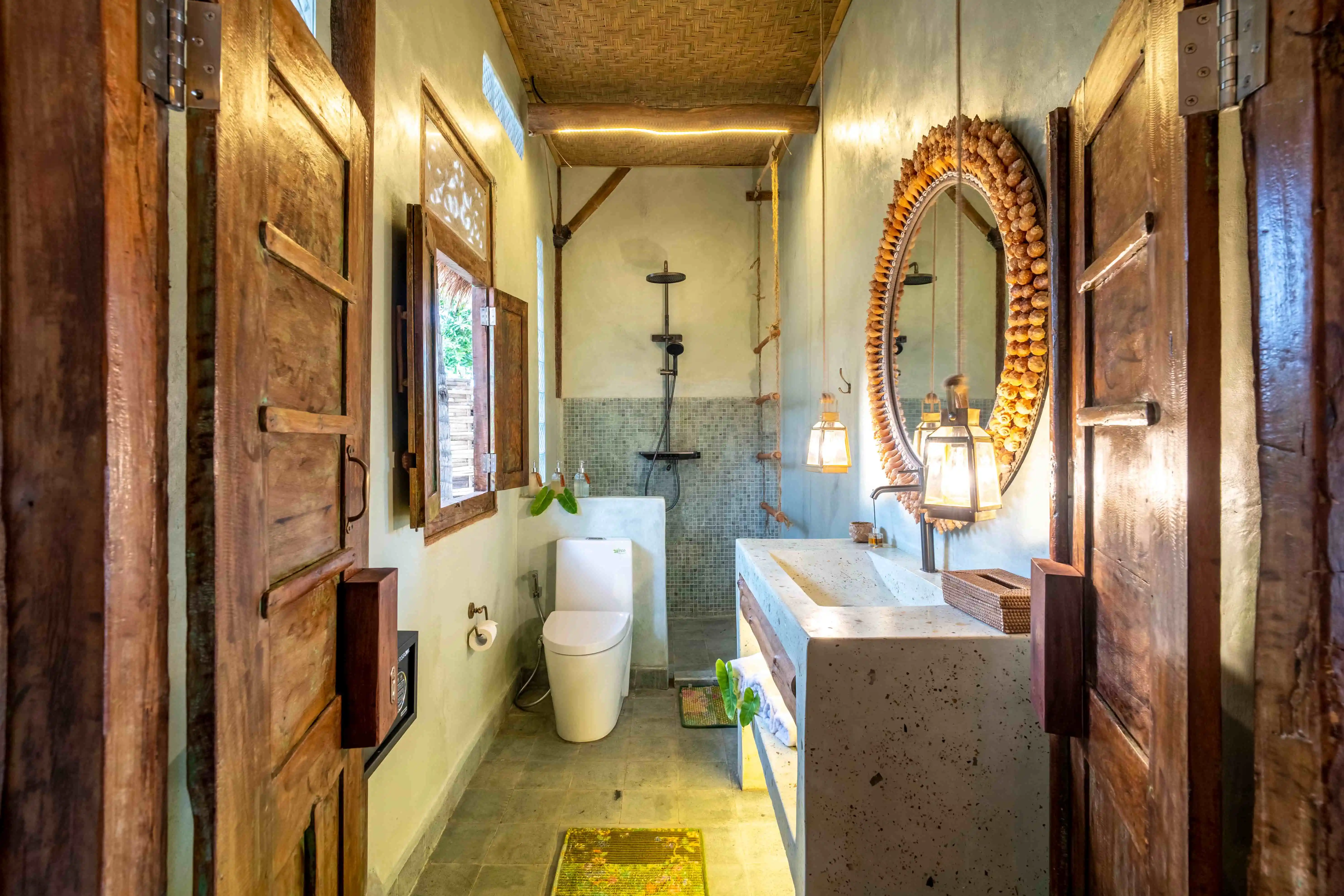 Elegant villa bathroom featuring a handcrafted stone vanity, rustic wooden doors, and a walk-in rainfall shower.