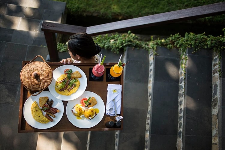 Overhead view of a server carrying a tray with breakfast items including omelets, eggs Benedict, hash browns, and fresh juices.