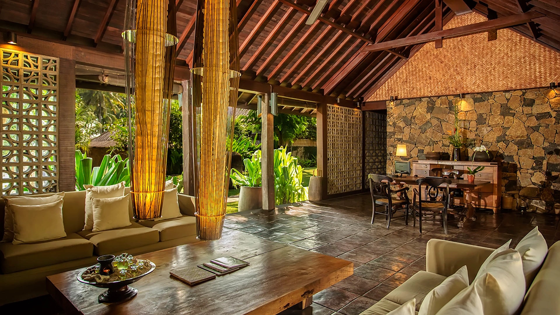 Spacious resort lobby lounge with high woven-wood ceilings, stone walls, low-slung sofas, and large decorative bamboo lanterns.