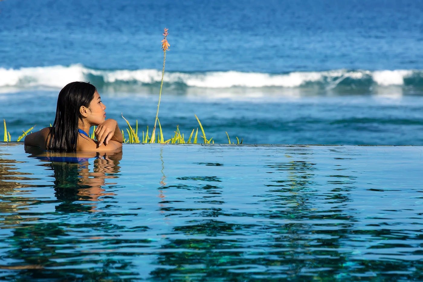 Guest resting at the edge of an infinity pool overlooking breaking ocean waves.