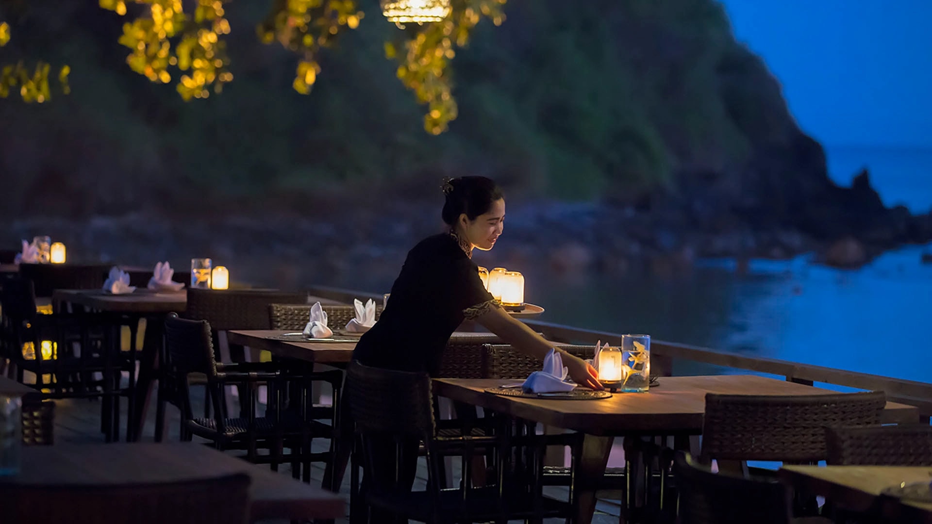 Evening beachfront dining deck with candlelit tables set up for a romantic dinner by the ocean.