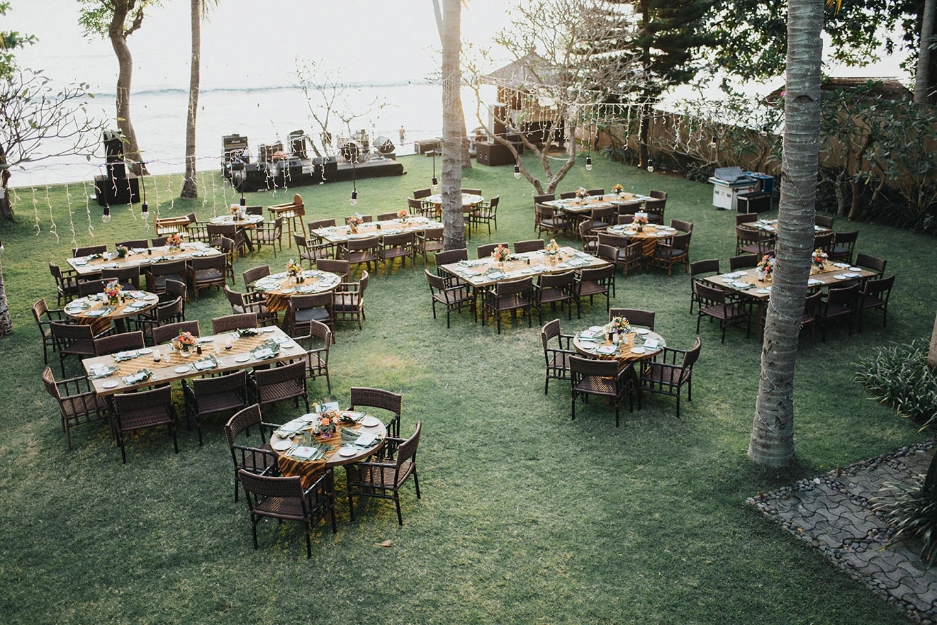 Overhead view of an outdoor wedding reception venue setup on a grassy lawn with dining tables and string lights near the beach.