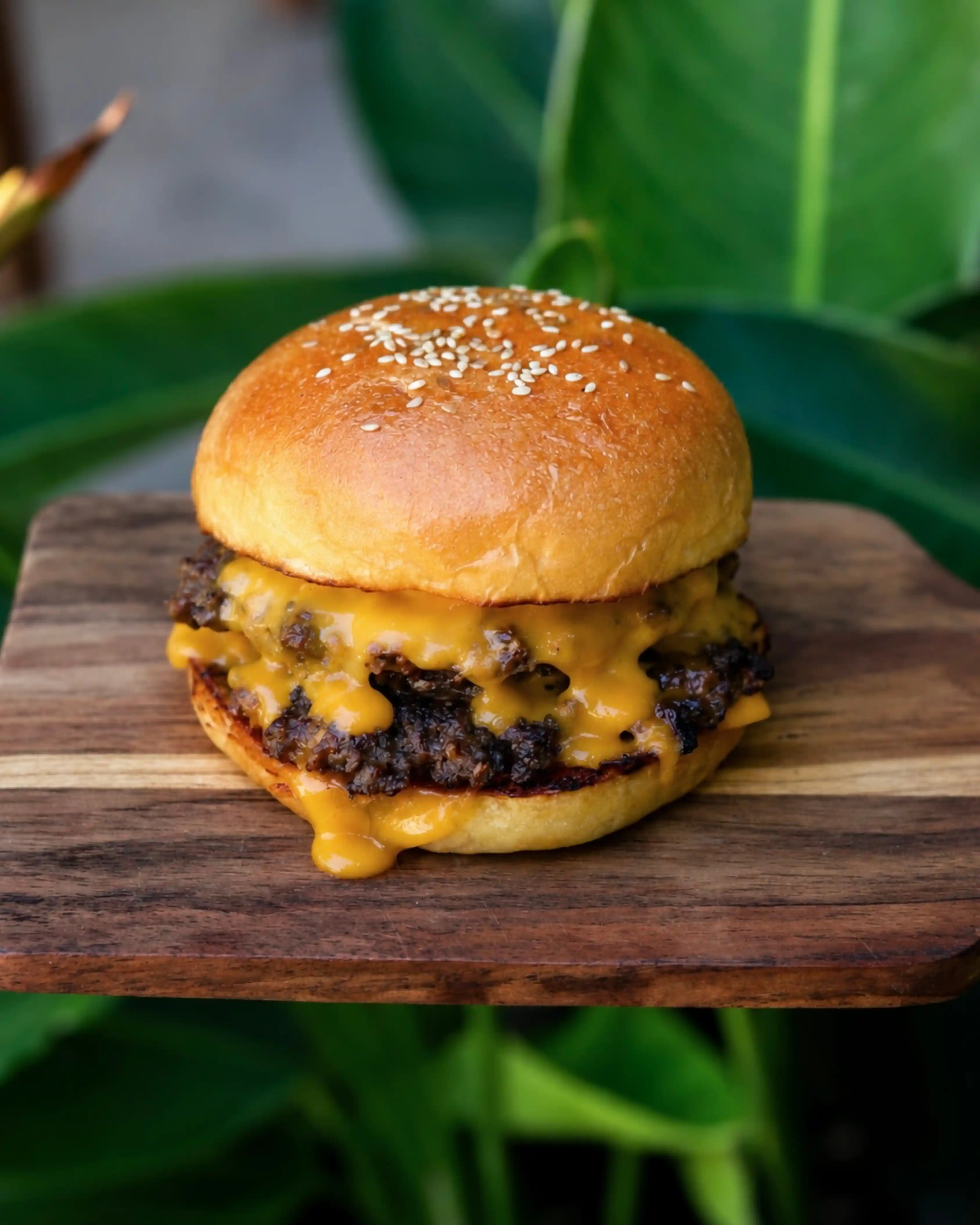A double cheeseburger with melted cheddar cheese dripping over two beef patties on a wooden serving board.