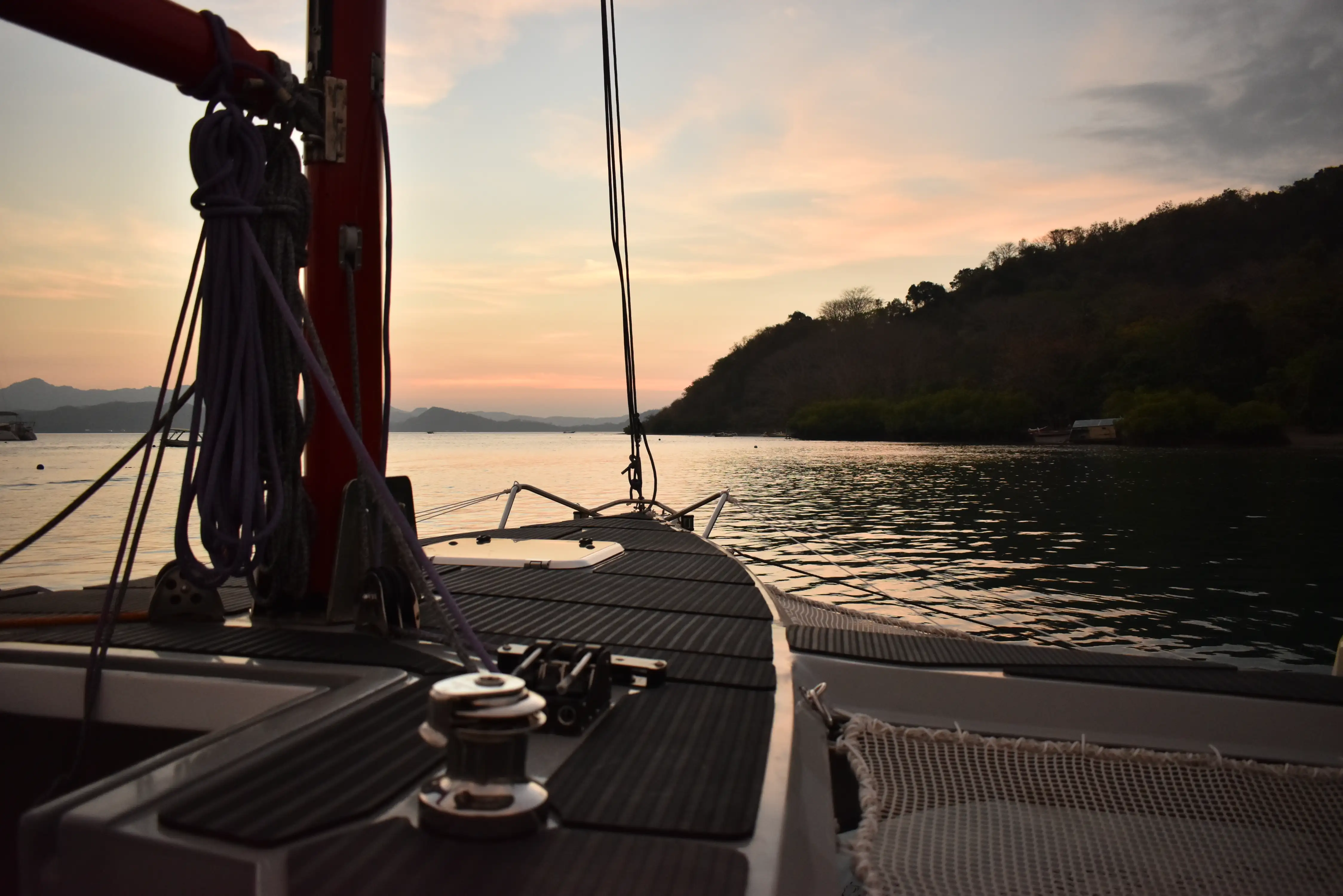View from the deck of a sailing trimaran pointing toward a calm bay during sunset.