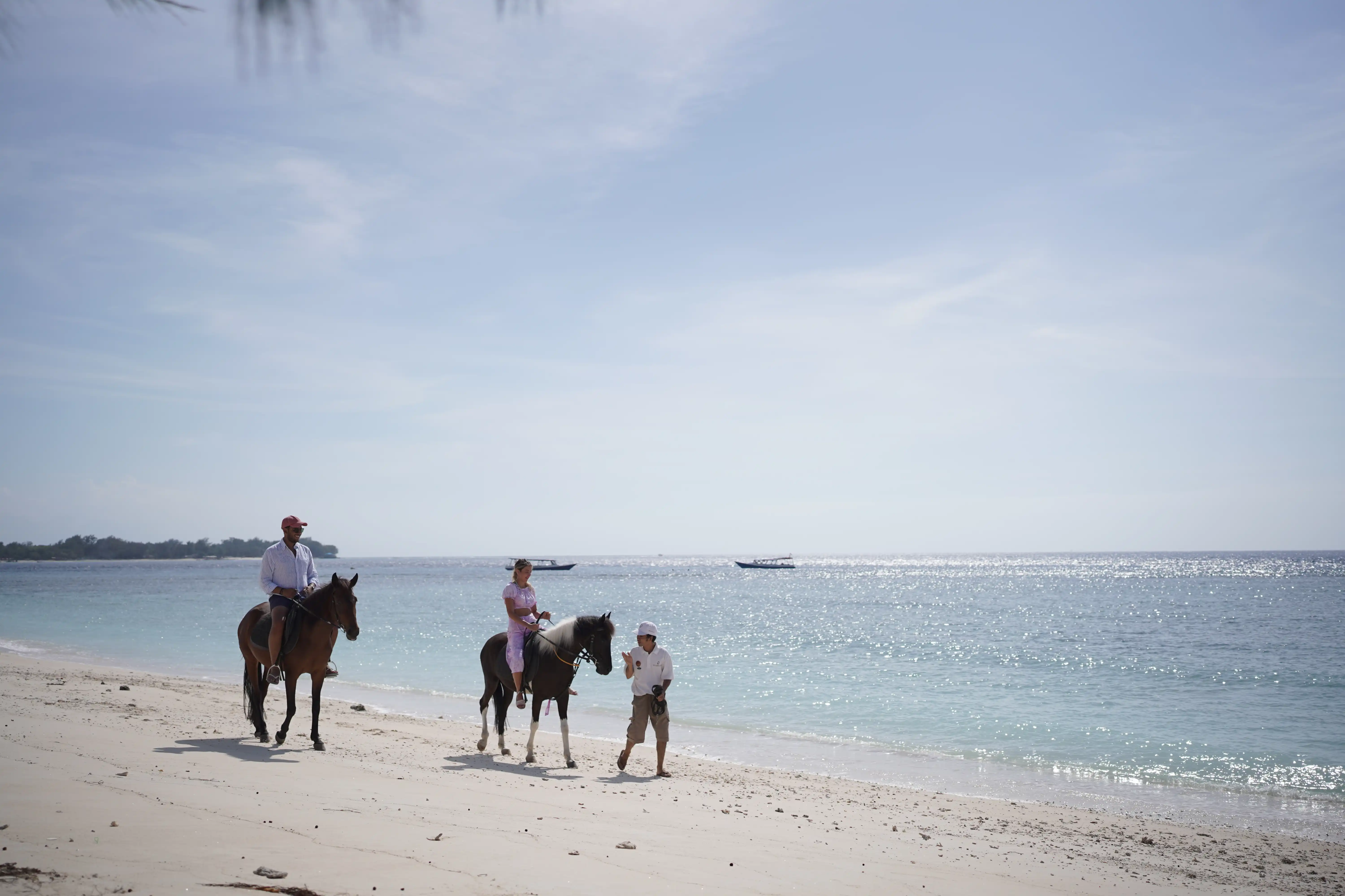 People horseback riding along a white sandy beach next to the blue ocean.