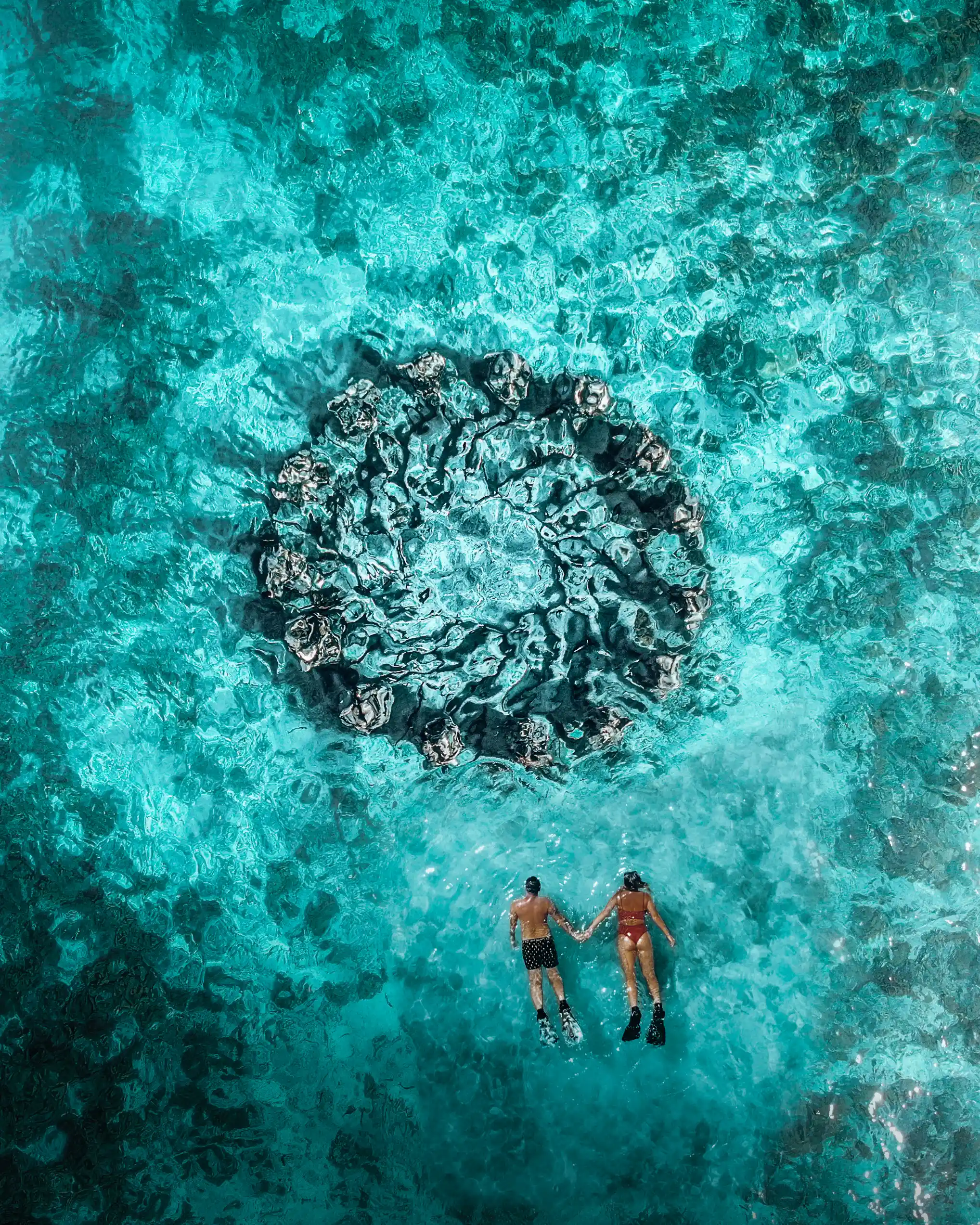 Aerial view of two snorkelers swimming near an underwater circular statue installation in clear turquoise water.