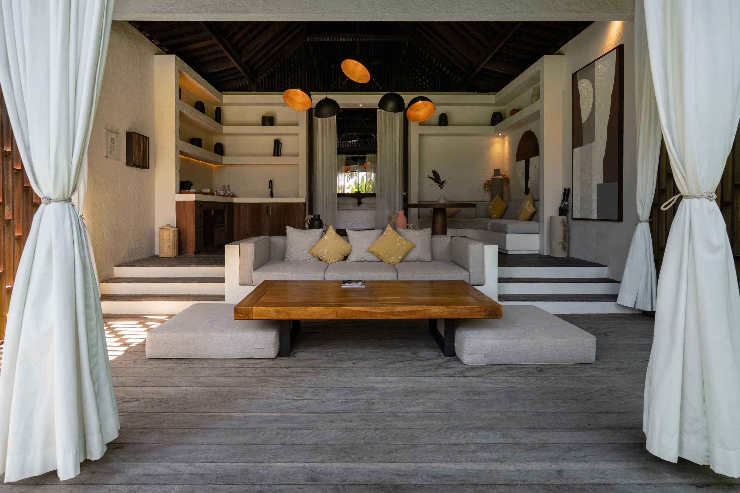 Open-concept outdoor lounge area with white curtains, plush seating, and neutral-toned modern decor.