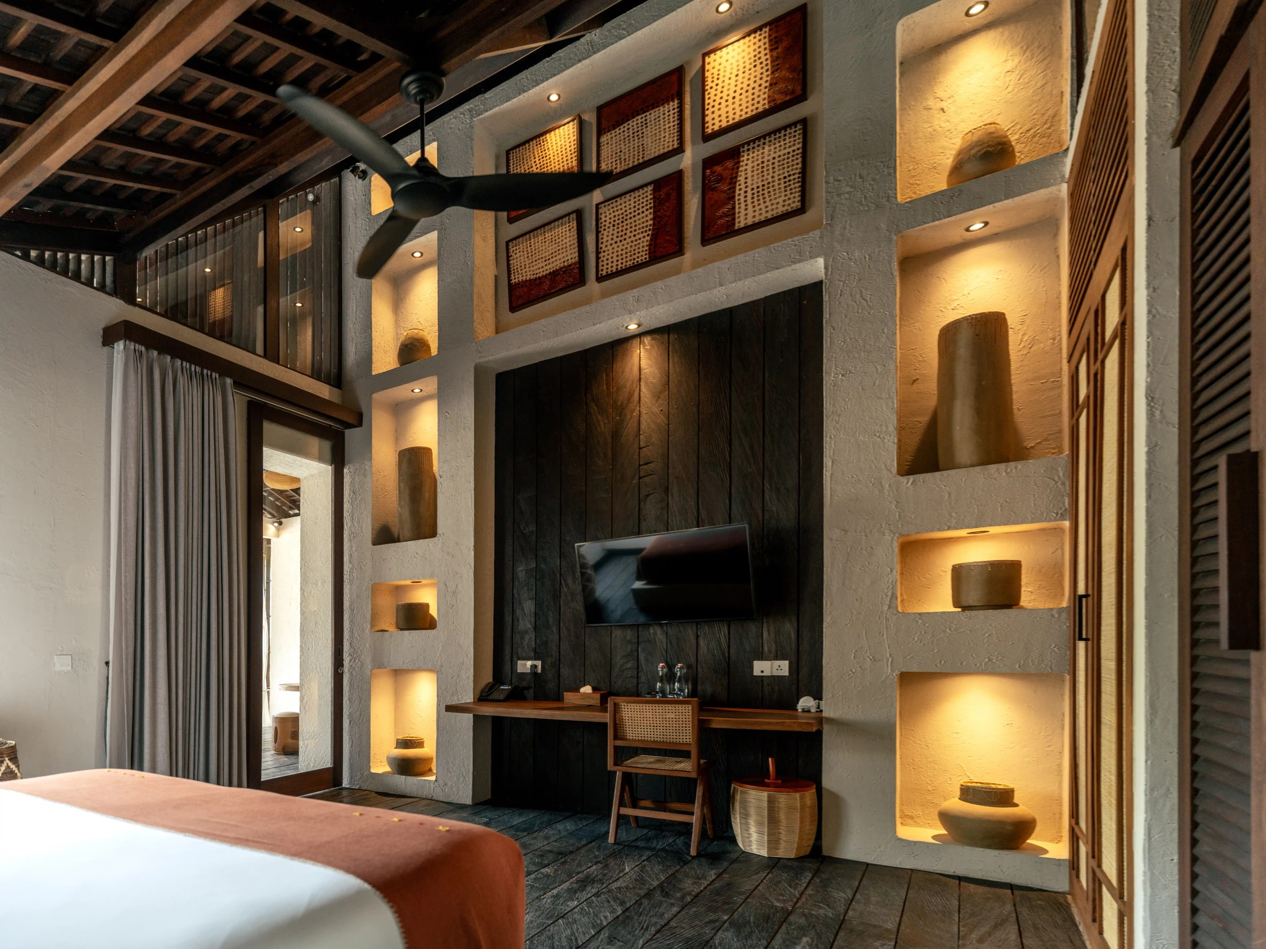 Modern resort bedroom featuring high ceilings, warm recessed lighting, and built-in display niches with pottery.