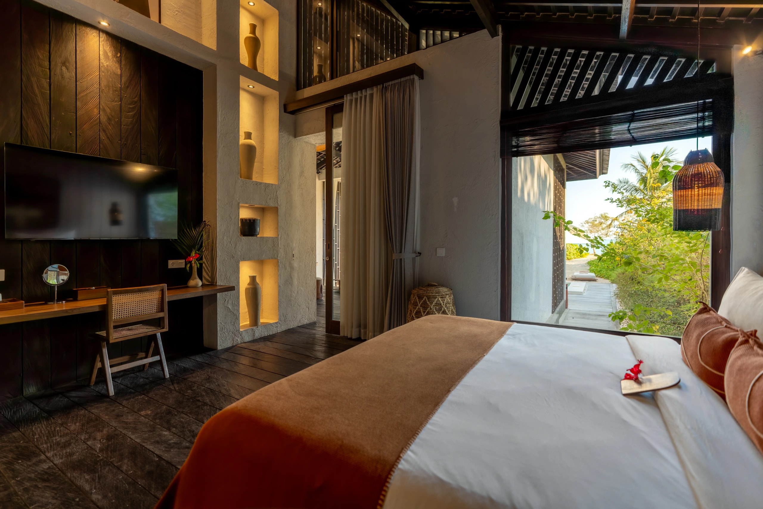 Spacious resort suite with a king-size bed, dark wood flooring, and large glass doors opening to a garden path.