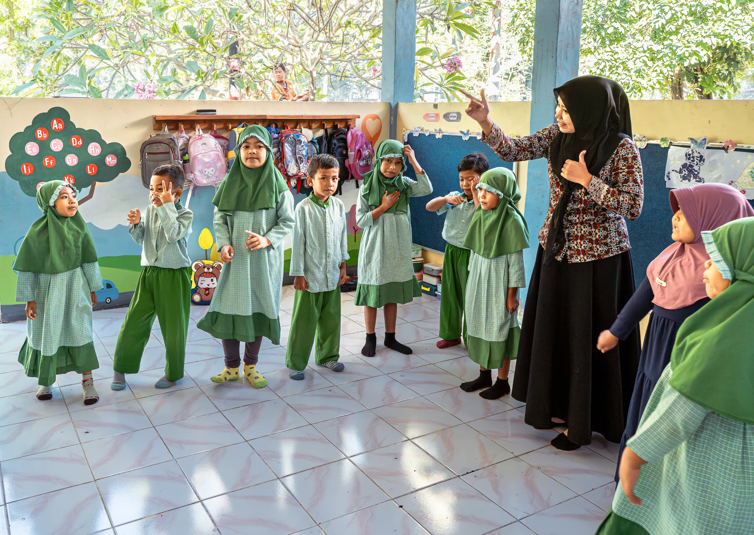 A teacher guiding a group of young school children standing in a classroom line during an activity.