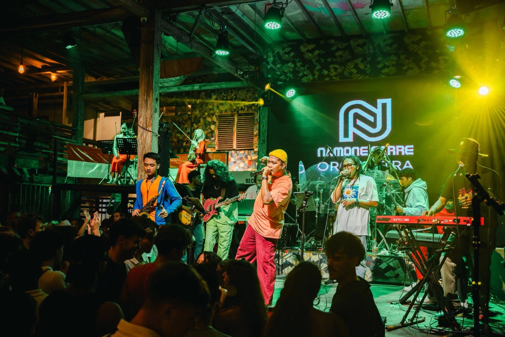 Band performing on stage under green and yellow lights at a rustic venue.