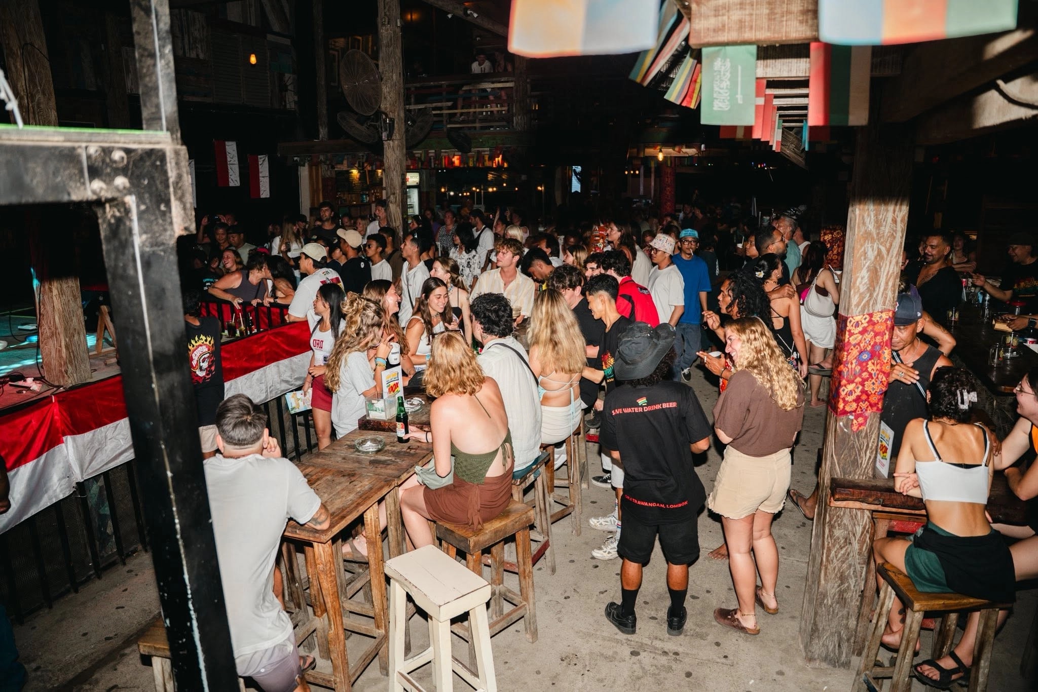 People socializing and drinking at wooden high-top tables in a bustling bar.