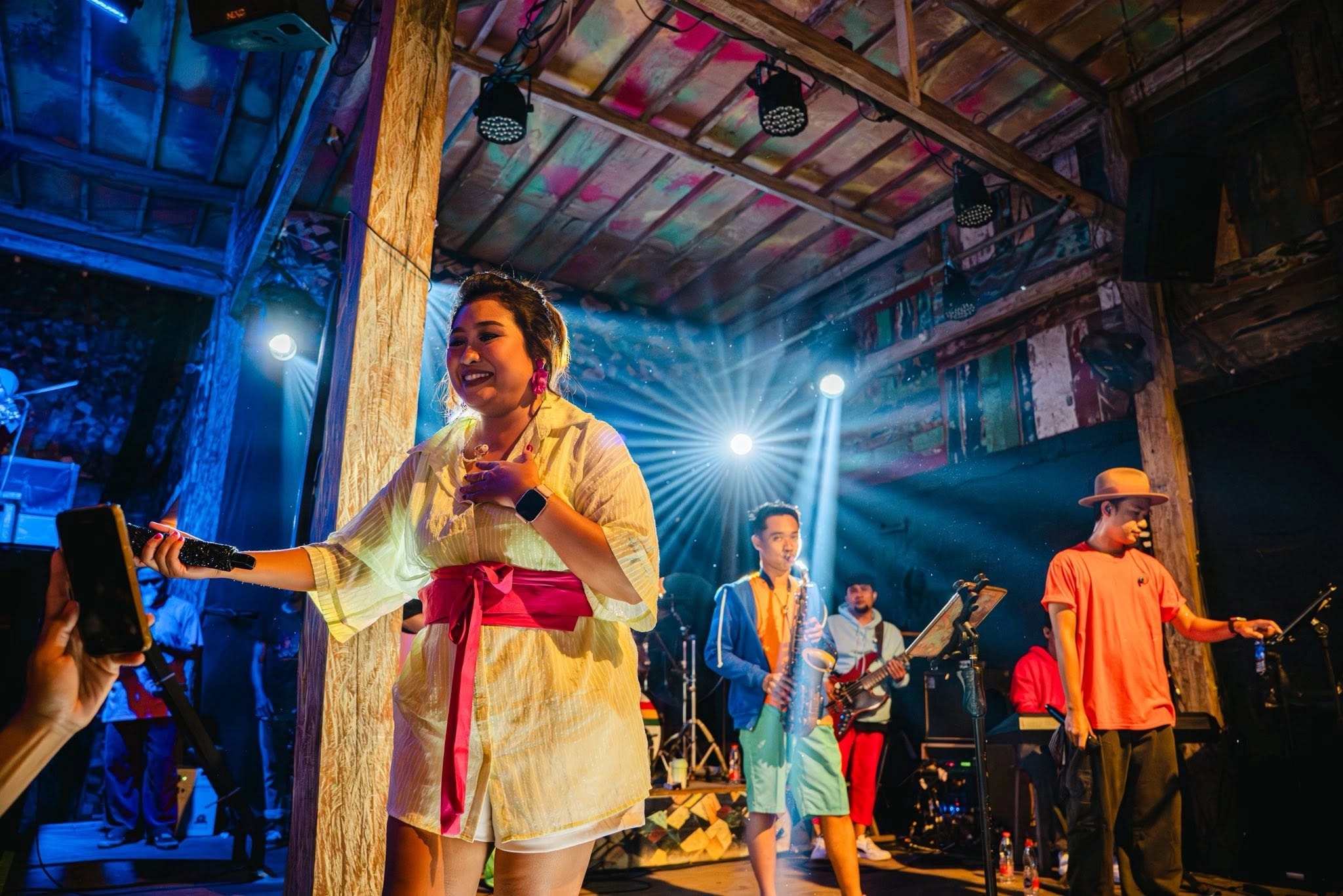 Vocalist in a white outfit performing on stage under bright spotlights with her band.