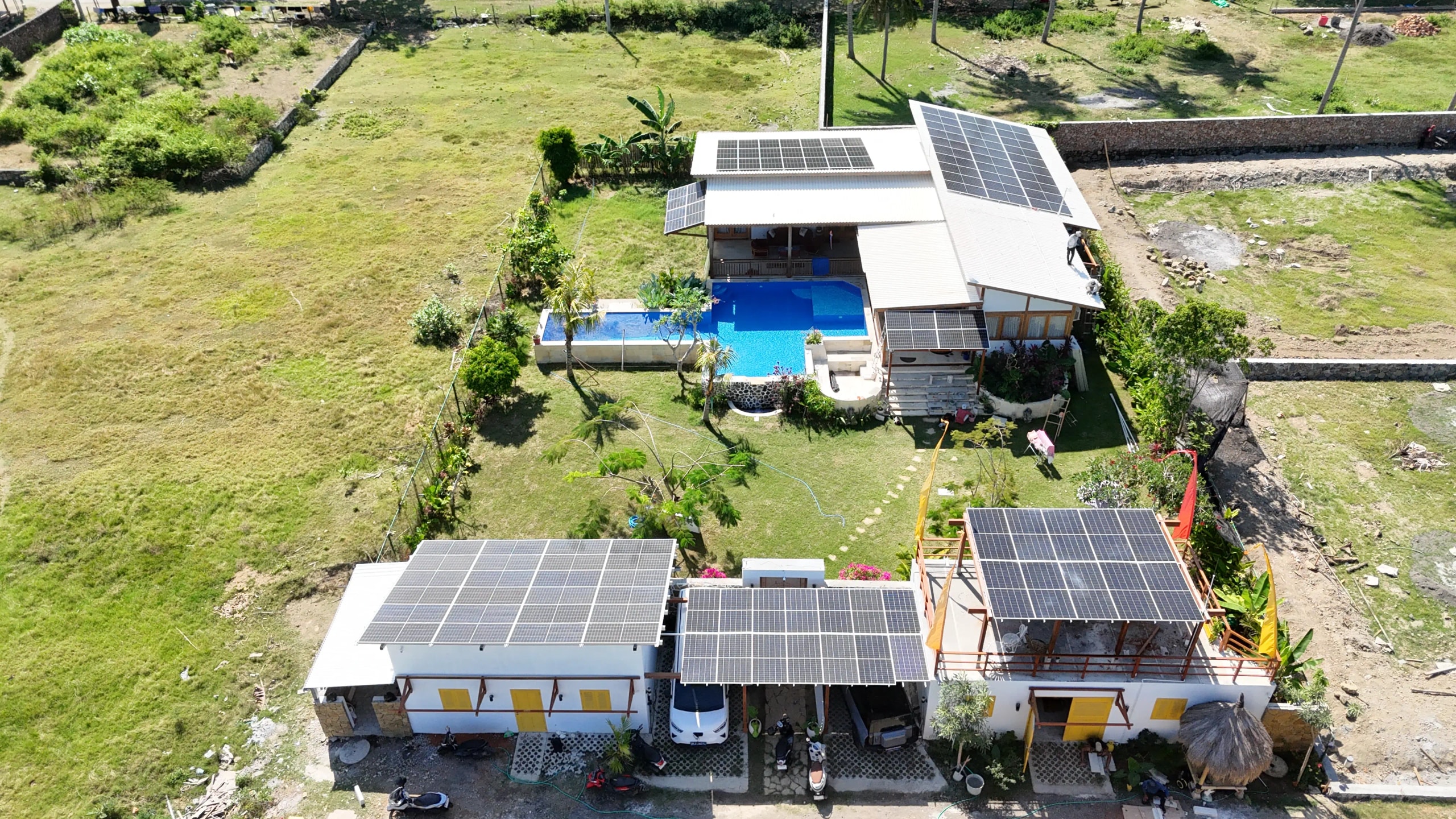 : Aerial shot of a luxury villa compound featuring swimming pools and extensive rooftop solar panel installations.