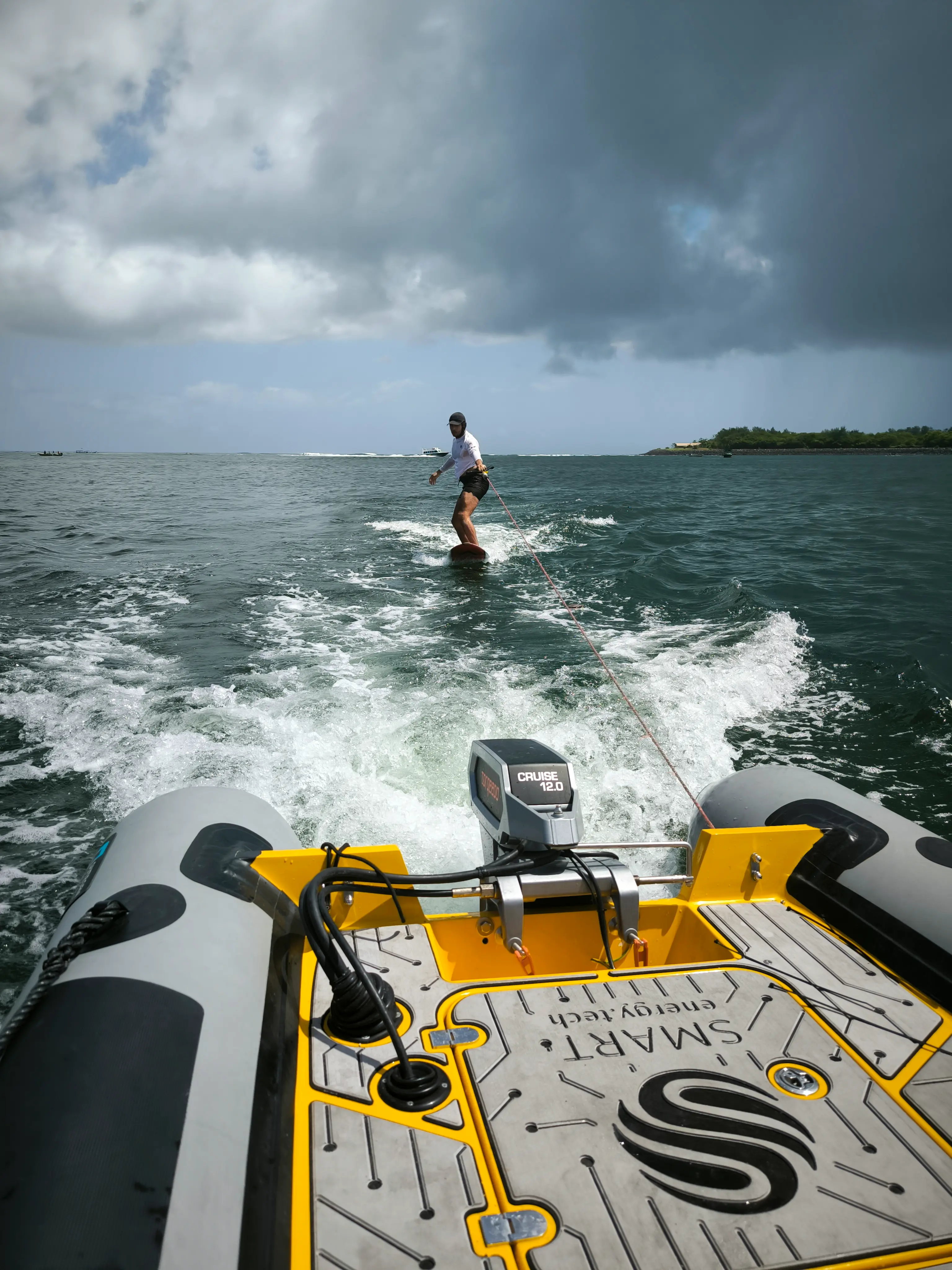 A wakeboarder being towed by a yellow electric boat across open sea water.