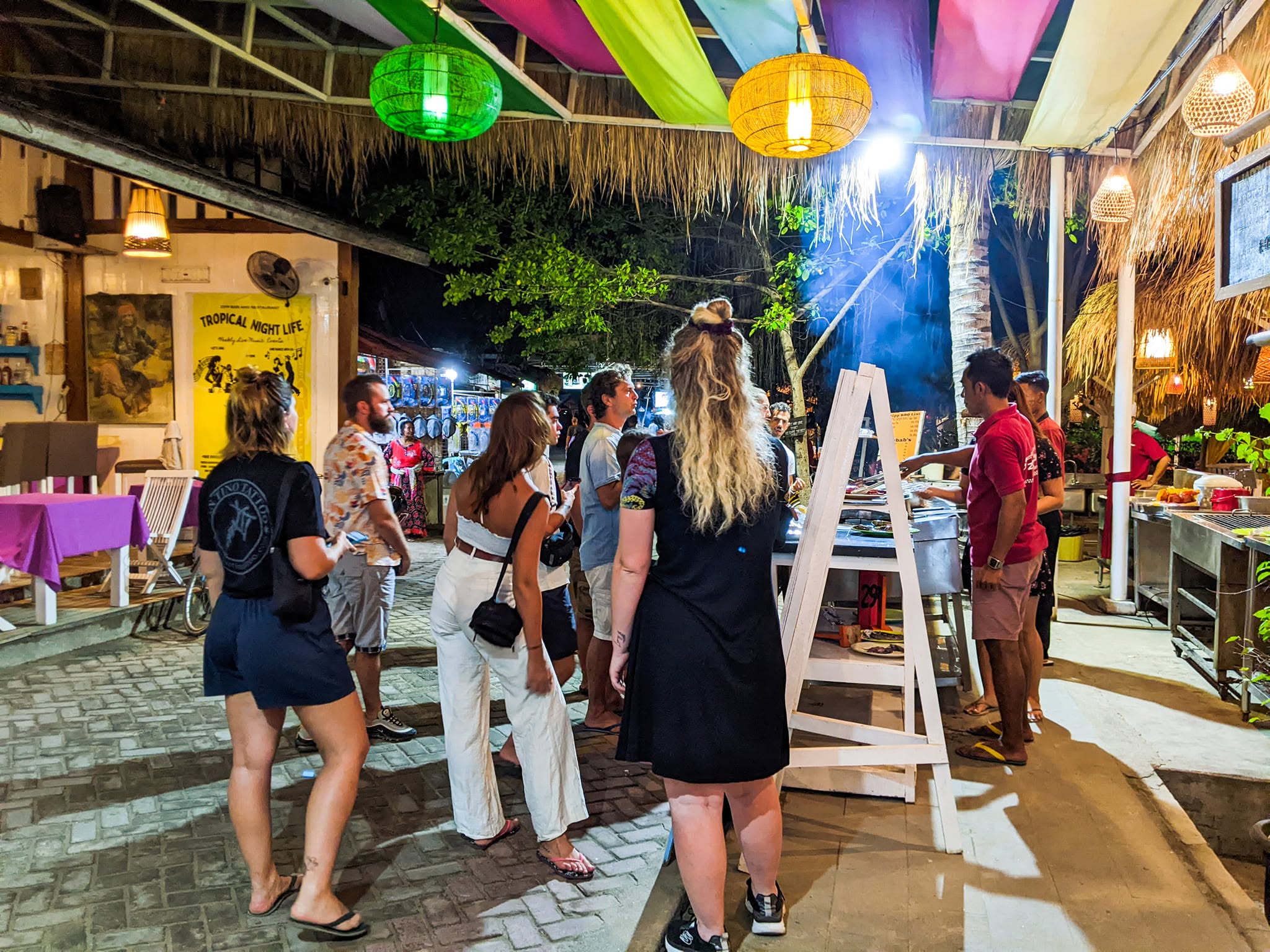 Guests gathered near a night food counter decorated with hanging lantern lights and fabric.