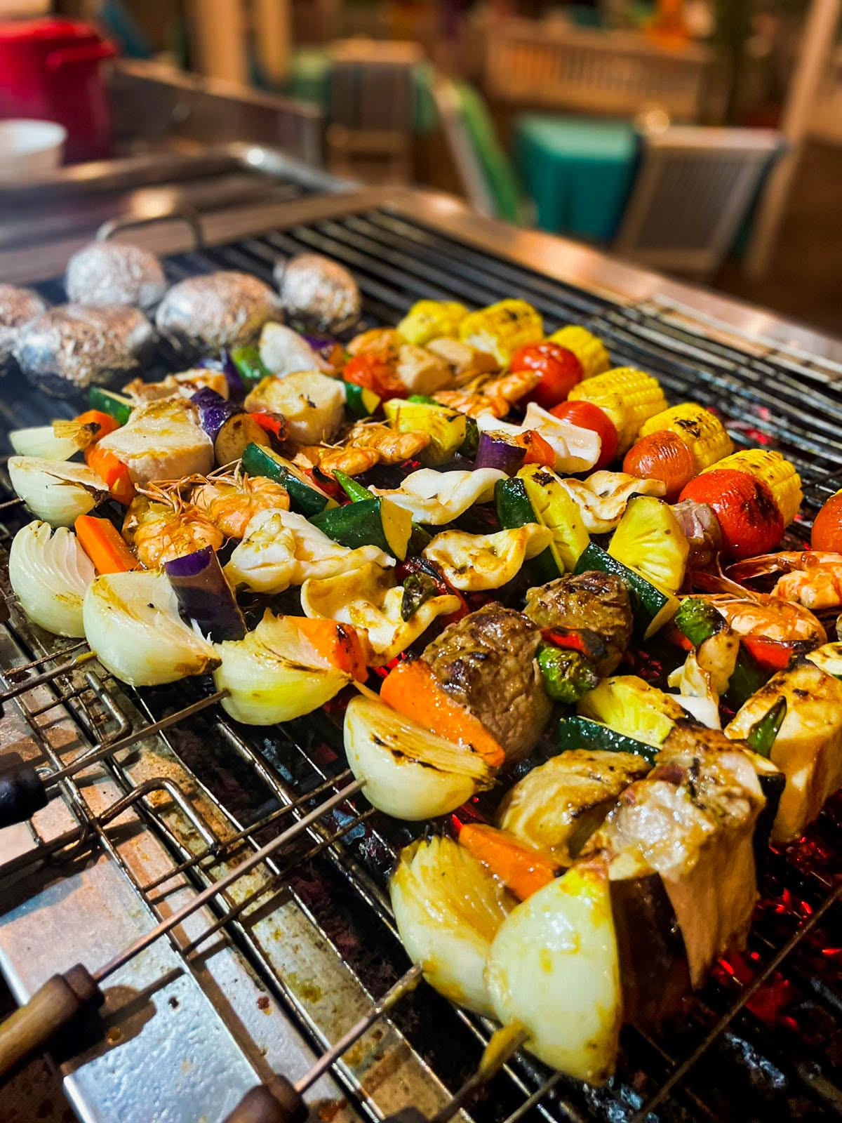 Close-up of mixed seafood, meat, and vegetable skewers grilling over hot coals.