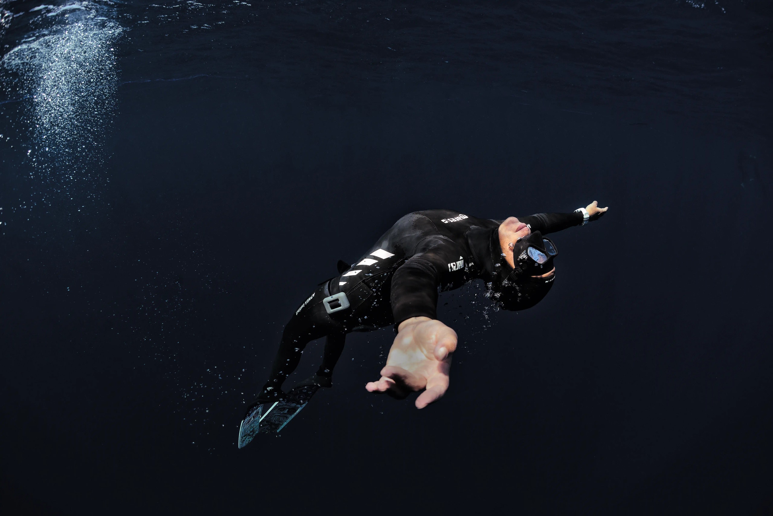 Diver wearing a black wetsuit backflipping into deep water.
