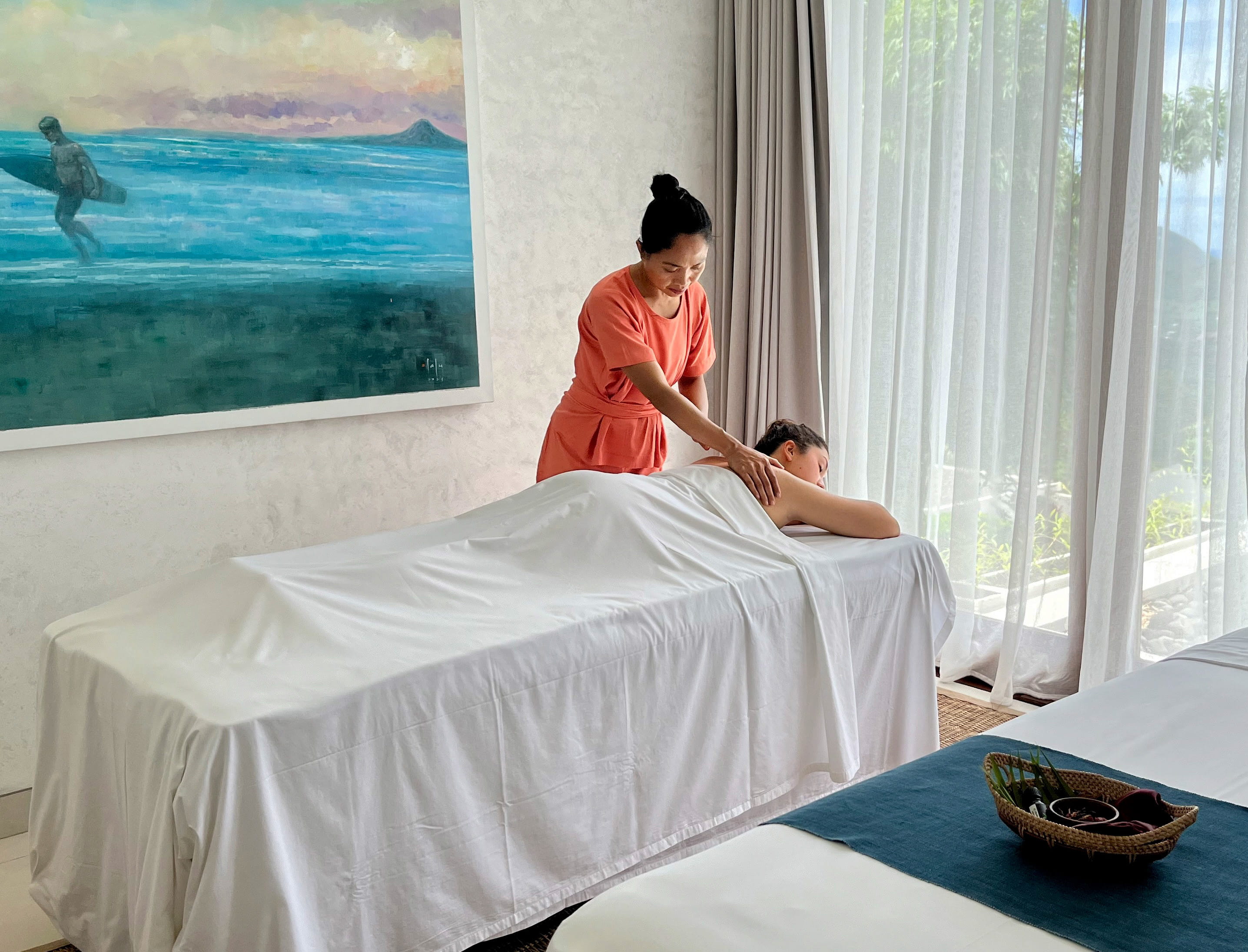 Spa therapist giving a relaxing massage to a client on a treatment bed in a bright, tranquil room.