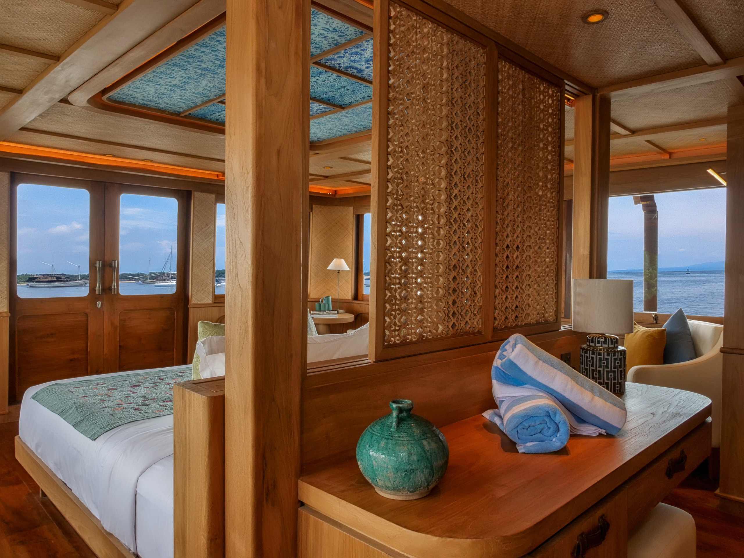 Luxury cabin interior of Jeeva Samudera Phinisi yacht featuring a king-size bed with traditional wooden accents and ocean views.