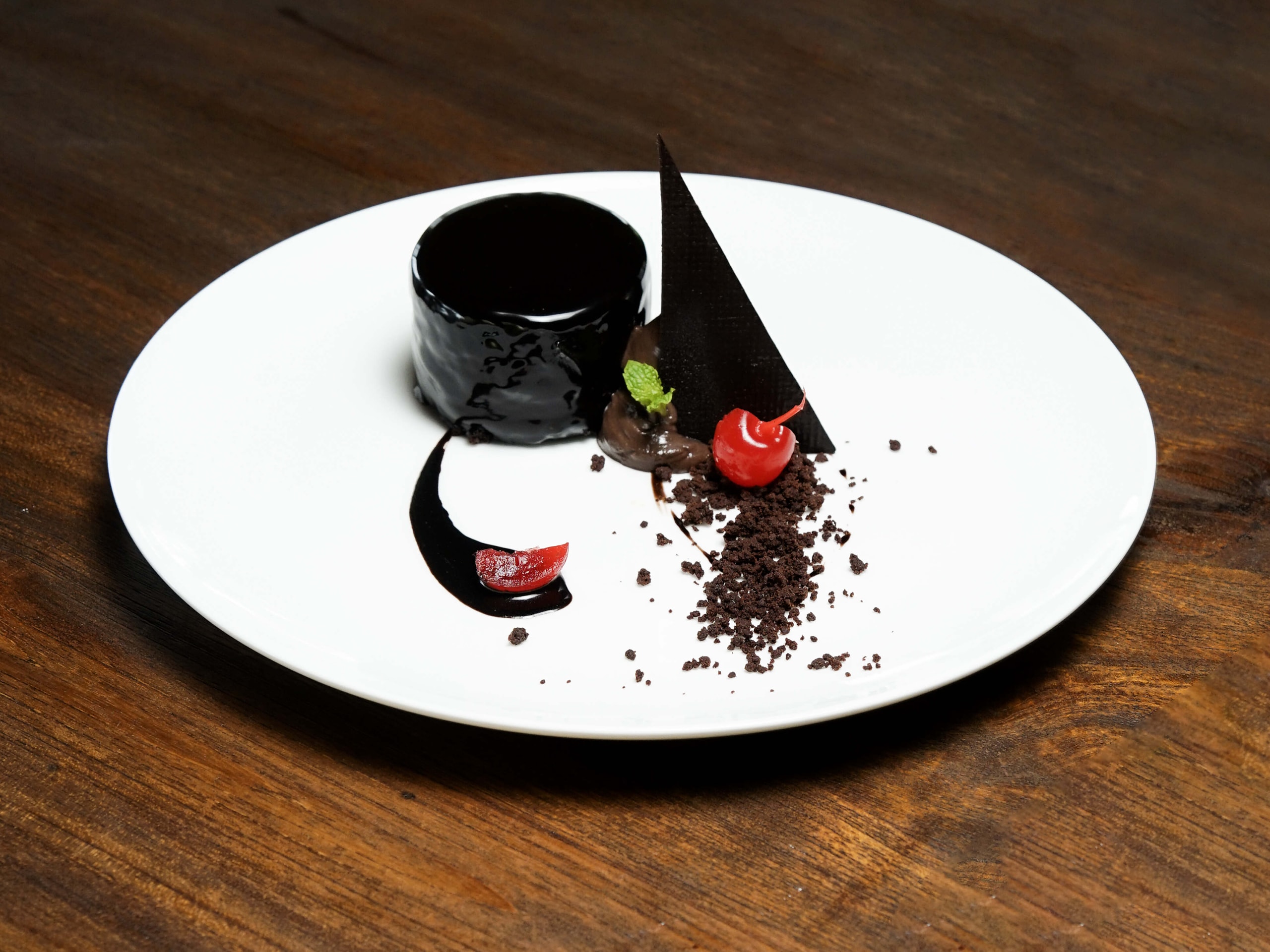 Gourmet plated Chocolate Date Cake by Chef Lalu Nasir, featuring a high-gloss chocolate glaze, fresh cherry, chocolate soil, and delicate chocolate garnish, with diced dates incorporated into the dish.