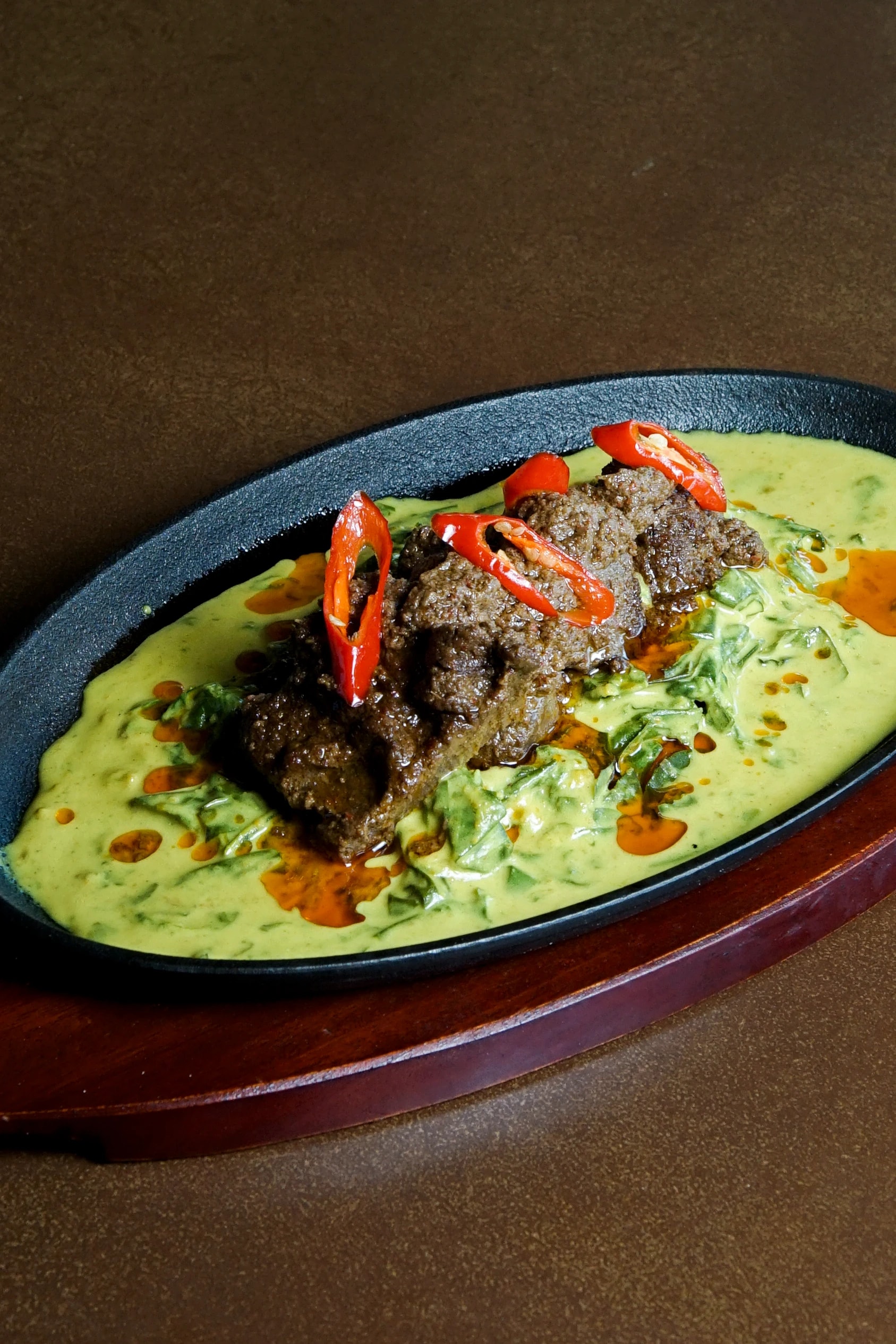 Beef rendang topped with sliced red chilies in yellow curry sauce on a sizzling cast-iron skillet.