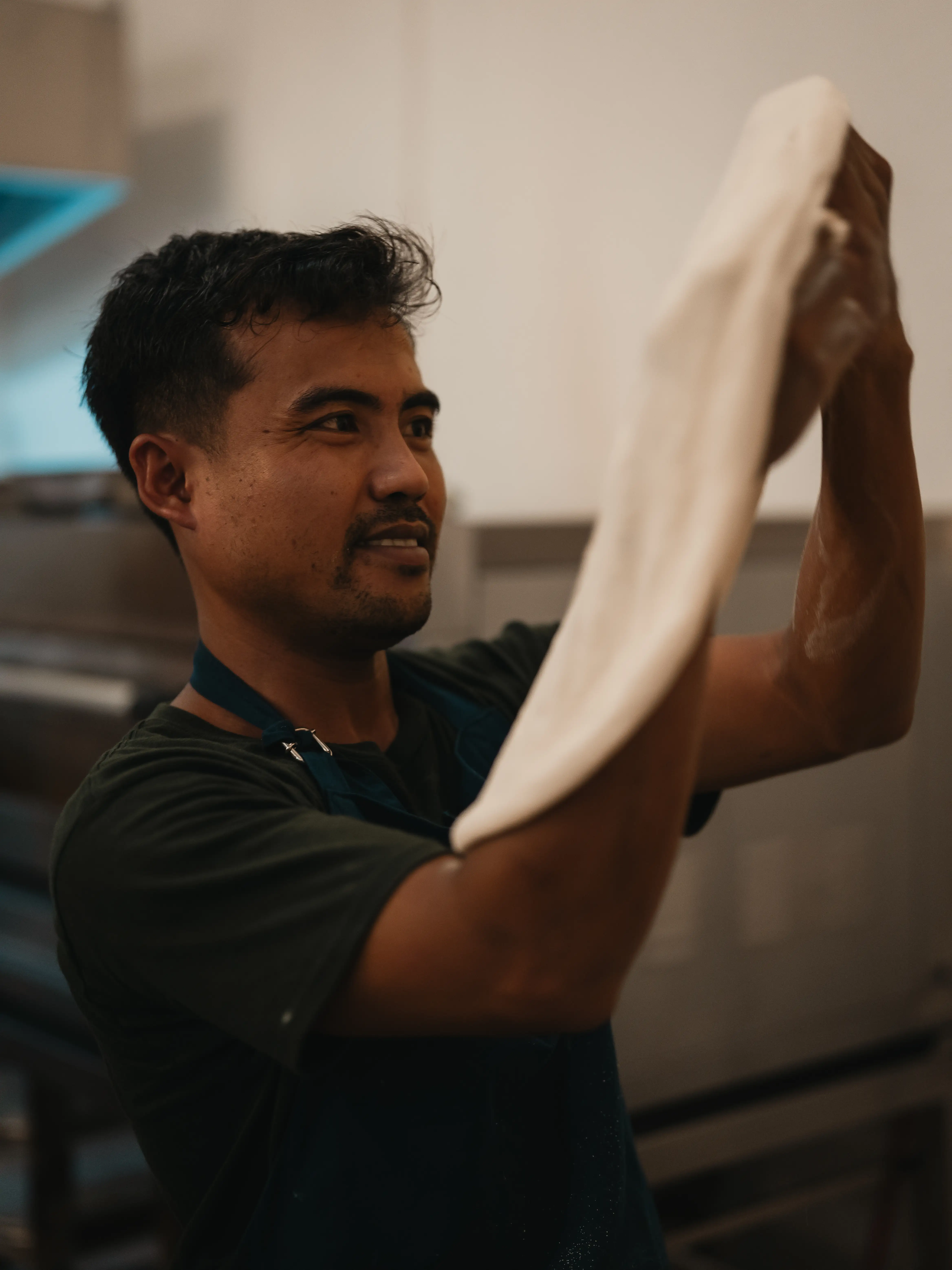 Chef in an apron stretching fresh pizza dough by hand in a restaurant kitchen.