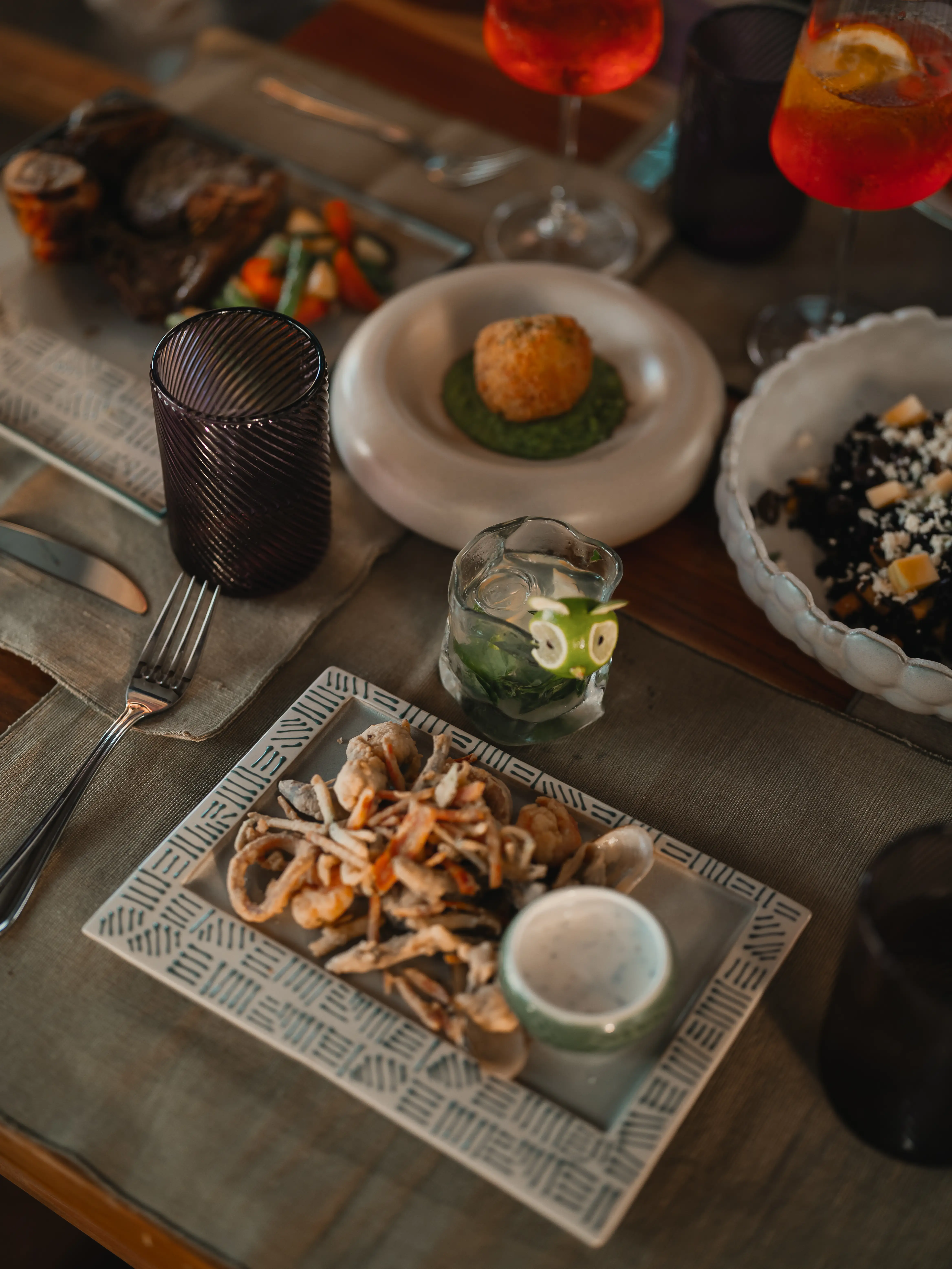 Gourmet spread of appetizers, fried seafood, and cocktails served on a restaurant table.