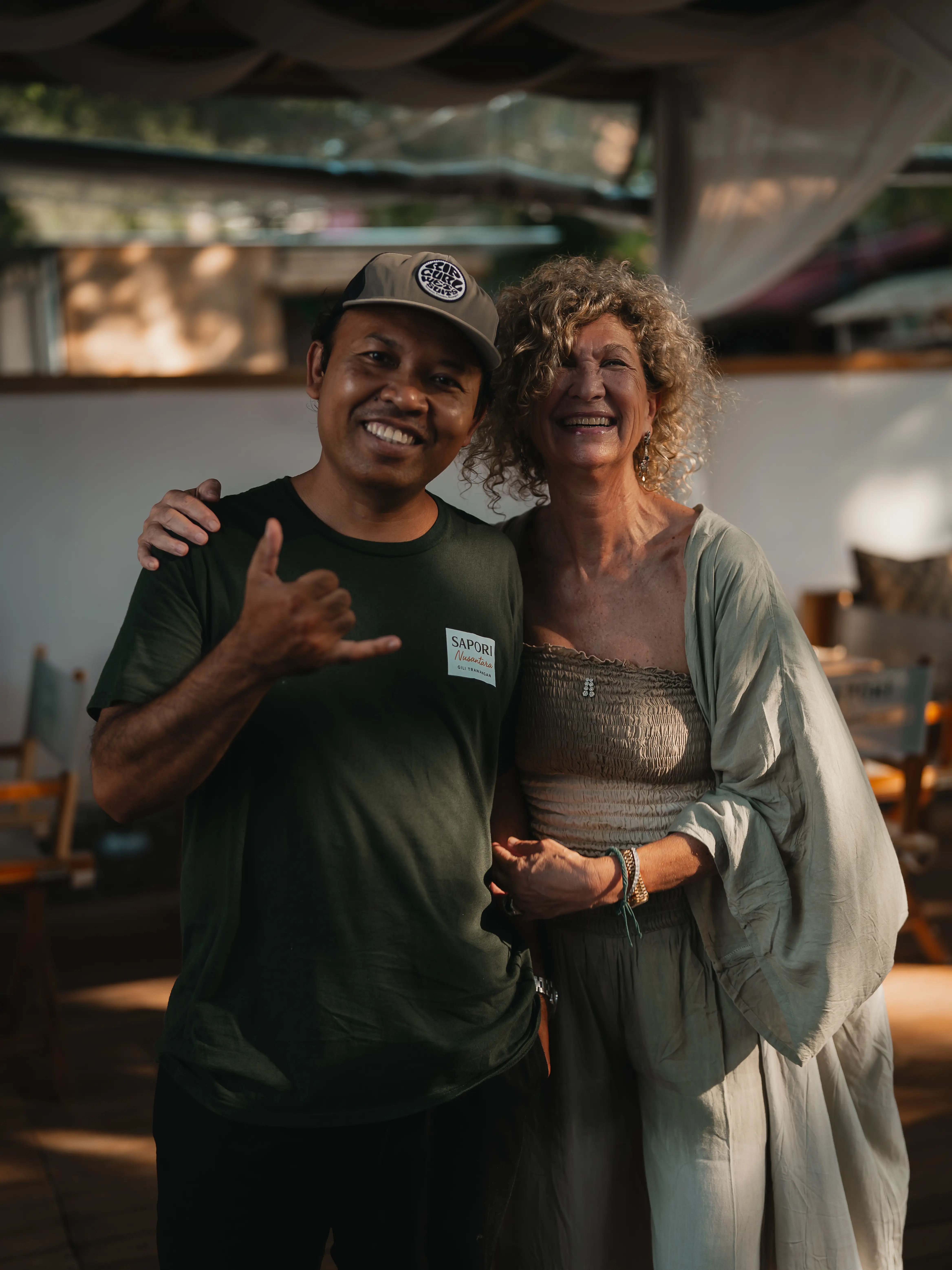 Man in a green shirt giving a hand gesture while posing alongside a smiling woman outdoors.