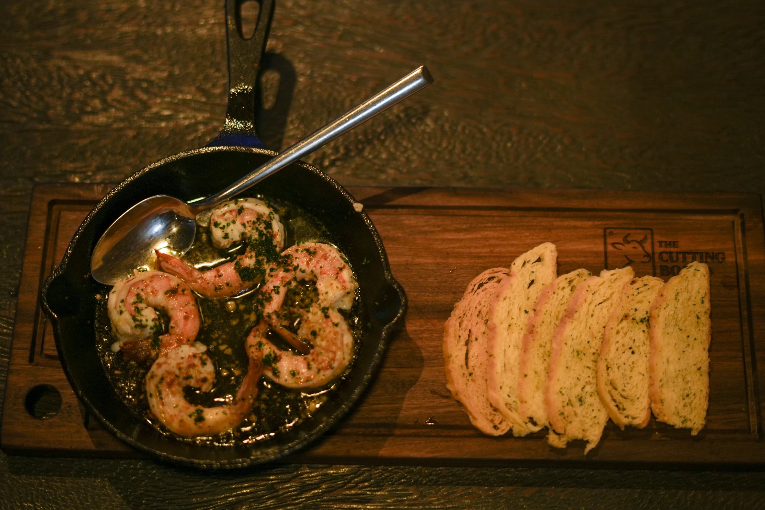 Garlic butter shrimp in a cast-iron skillet served with sliced toasted bread on a wooden board.