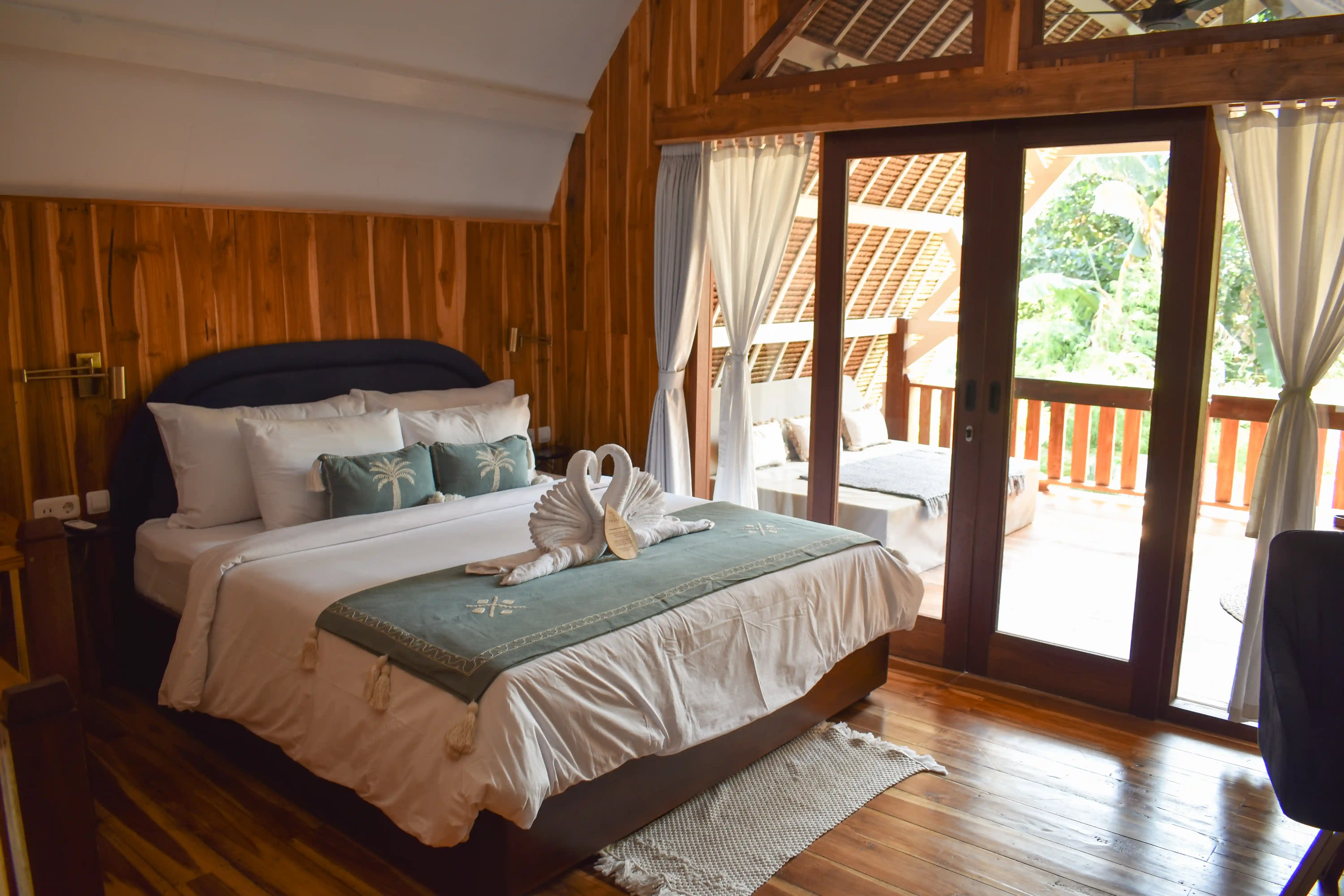 Cozy wooden bedroom featuring a king bed with towel swans and glass doors opening to a balcony.