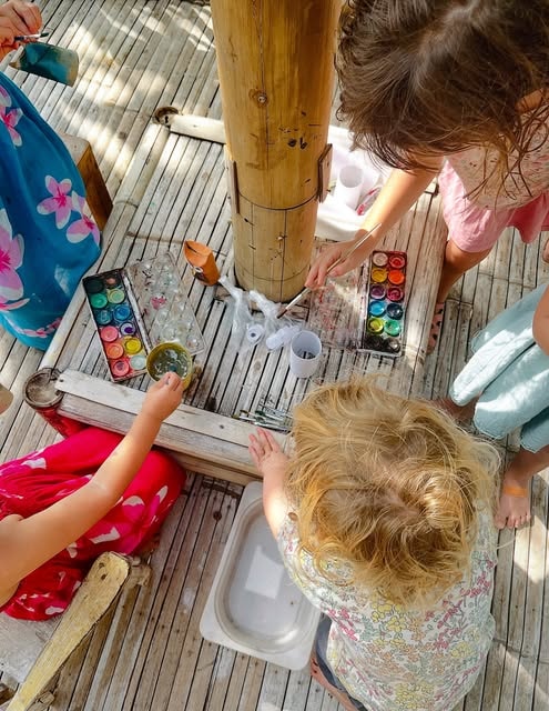 High-angle shot of young children gathered around a bamboo table using watercolor paints.