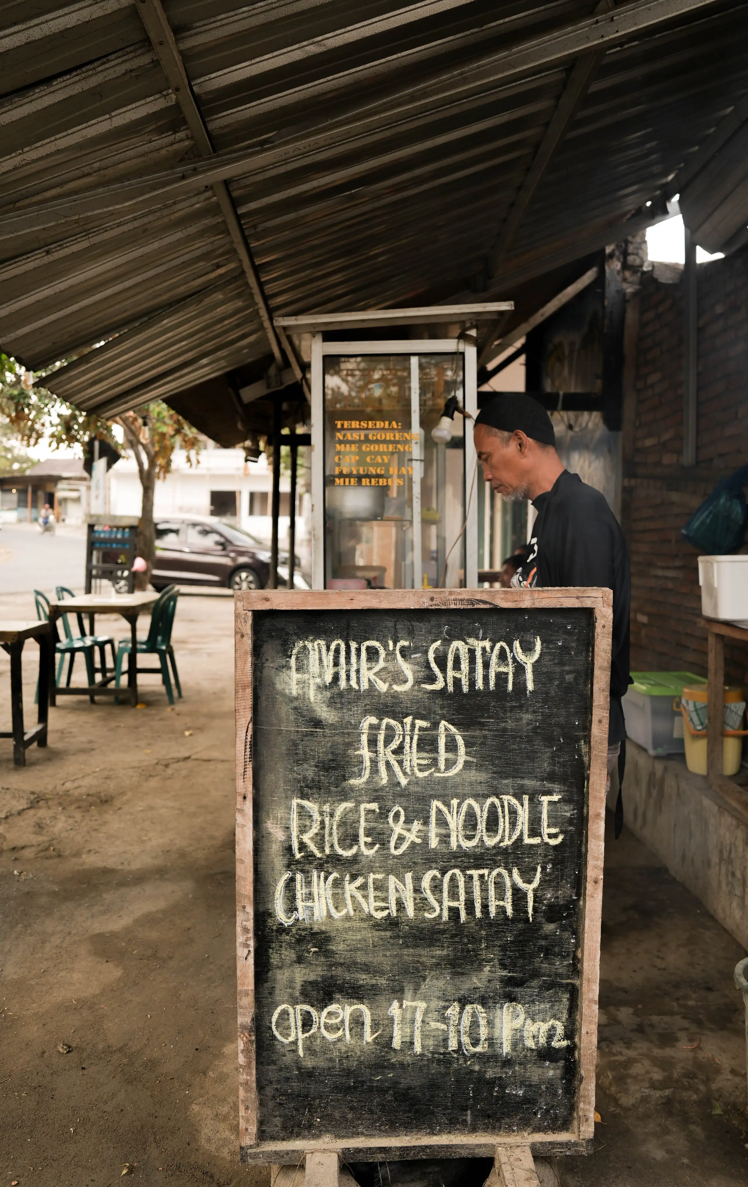 A wooden chalkboard menu sign for a local street food stall offering satay and fried rice.