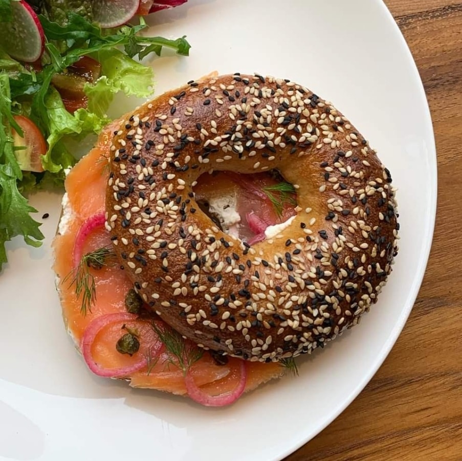 Smoked salmon bagel sandwich sprinkled with sesame seeds next to a side salad.