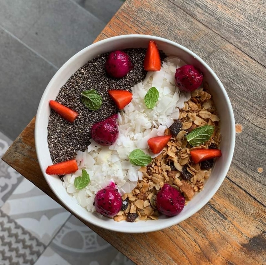 Smoothie bowl topped with chia seeds, coconut flakes, granola, strawberries, and dragon fruit.