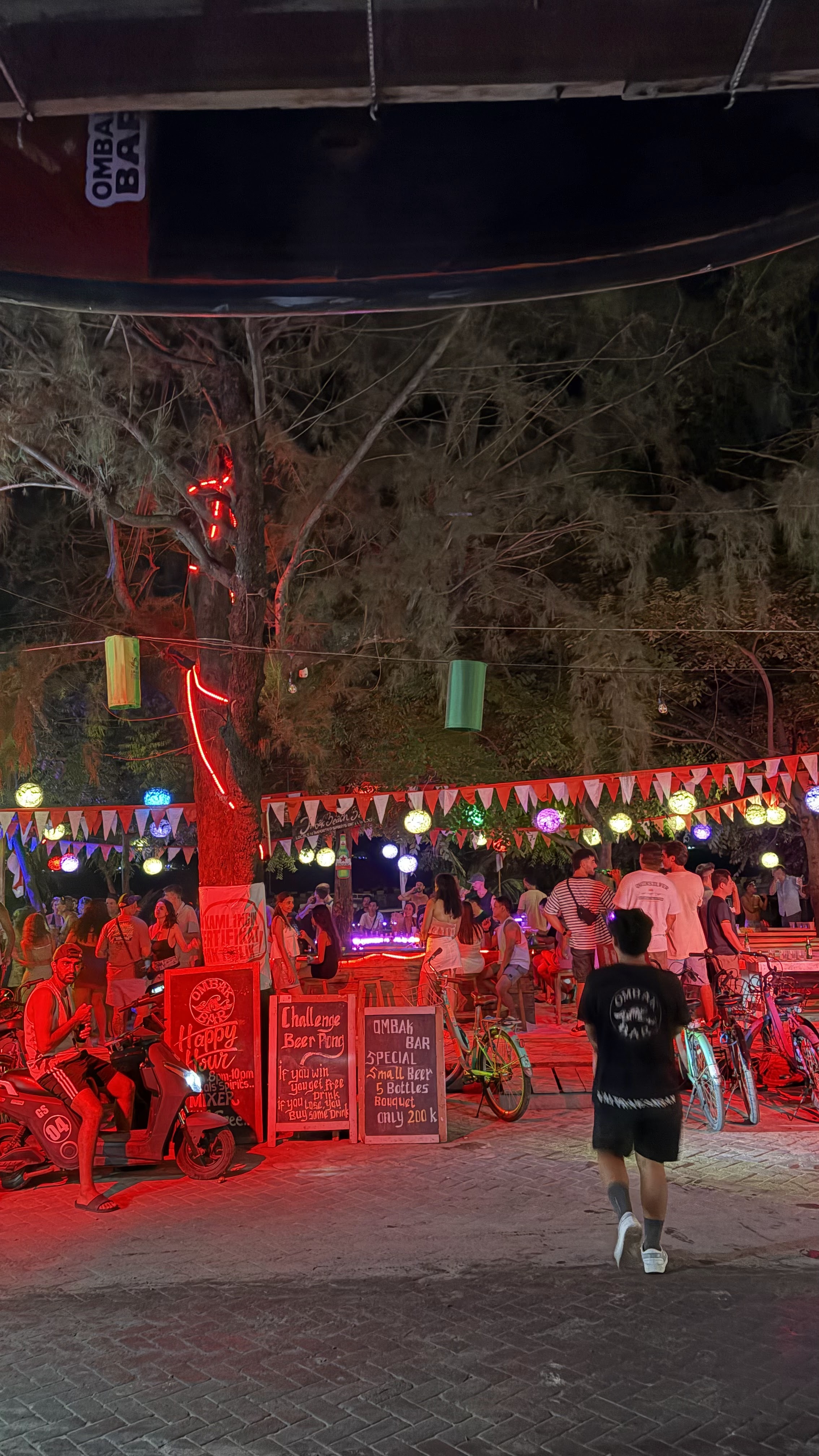 Entrance to an outdoor night bar decorated with string lights, red lanterns, and chalked menu boards.