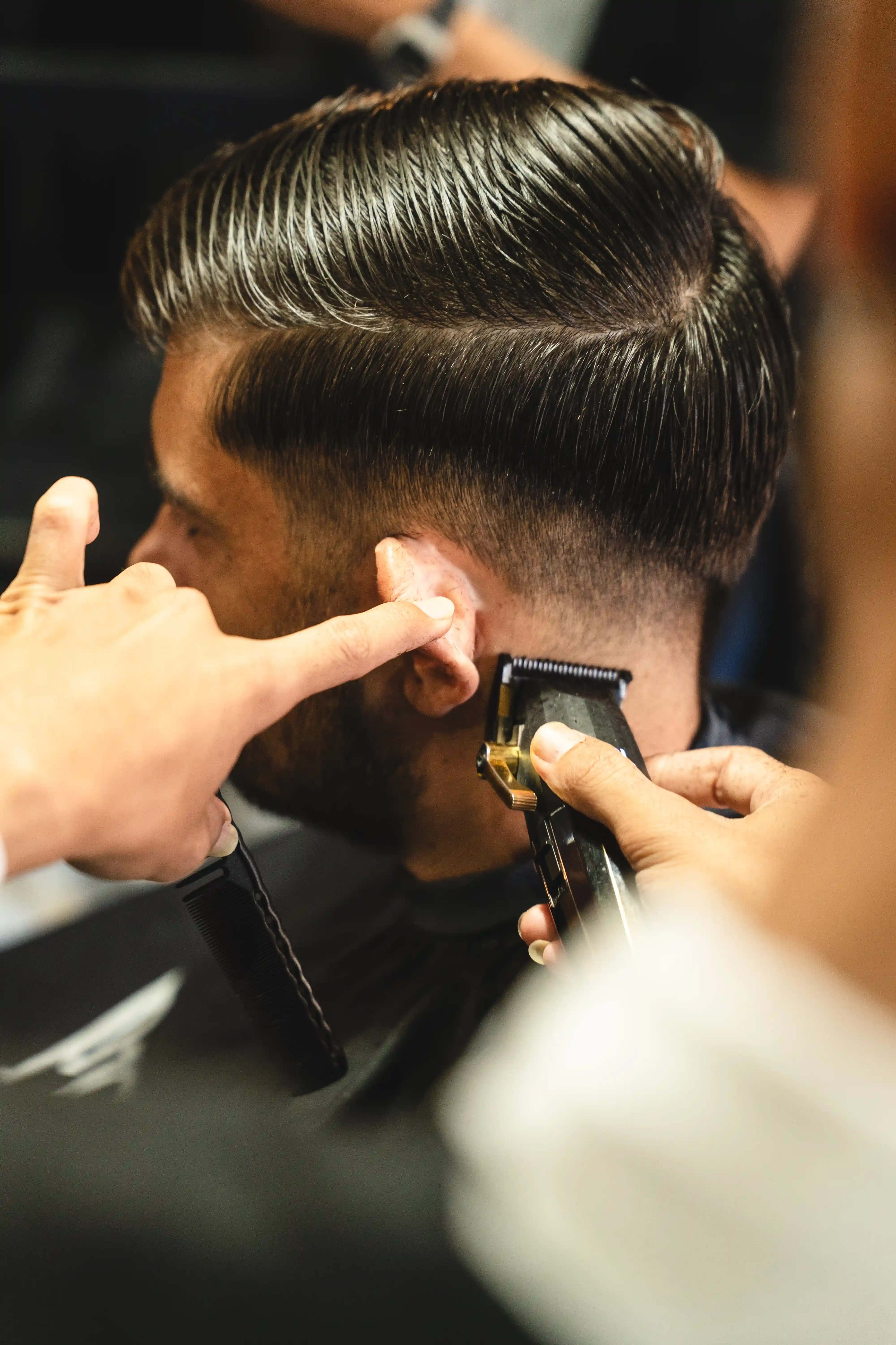 Barber using hair clippers to trim a client's sideburns and fade.