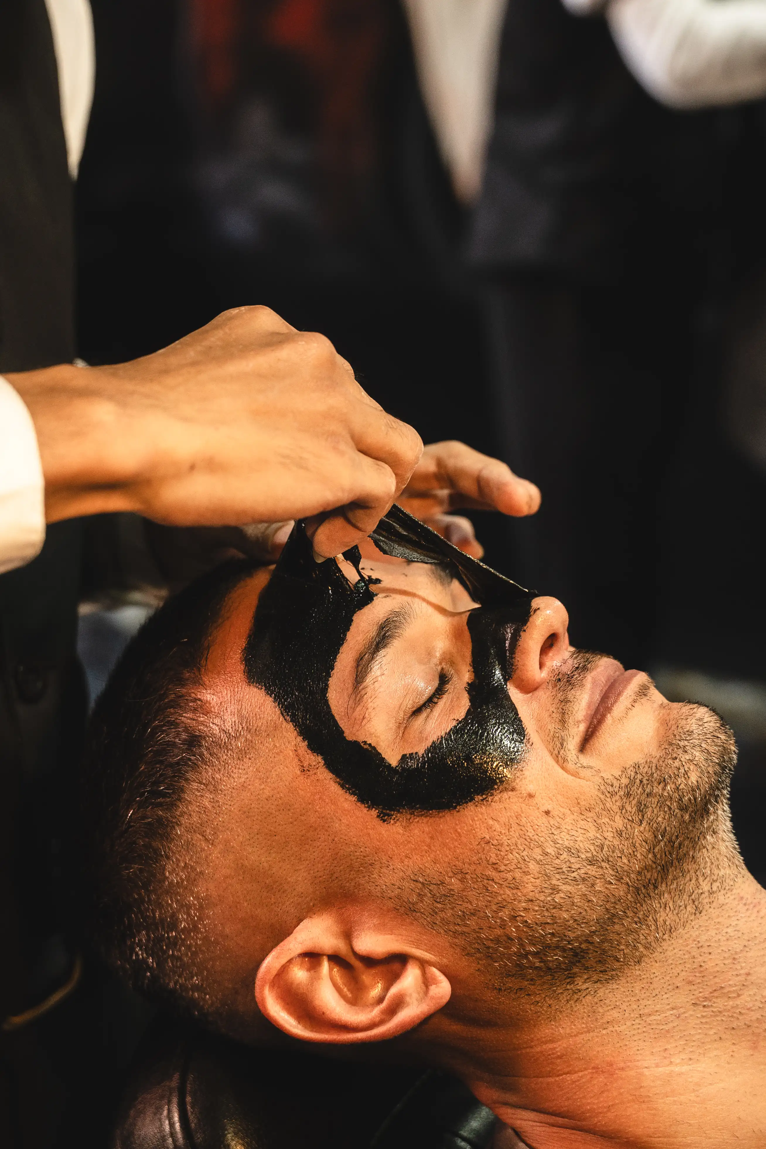 Man receiving a black peel-off face mask treatment at a barbershop.