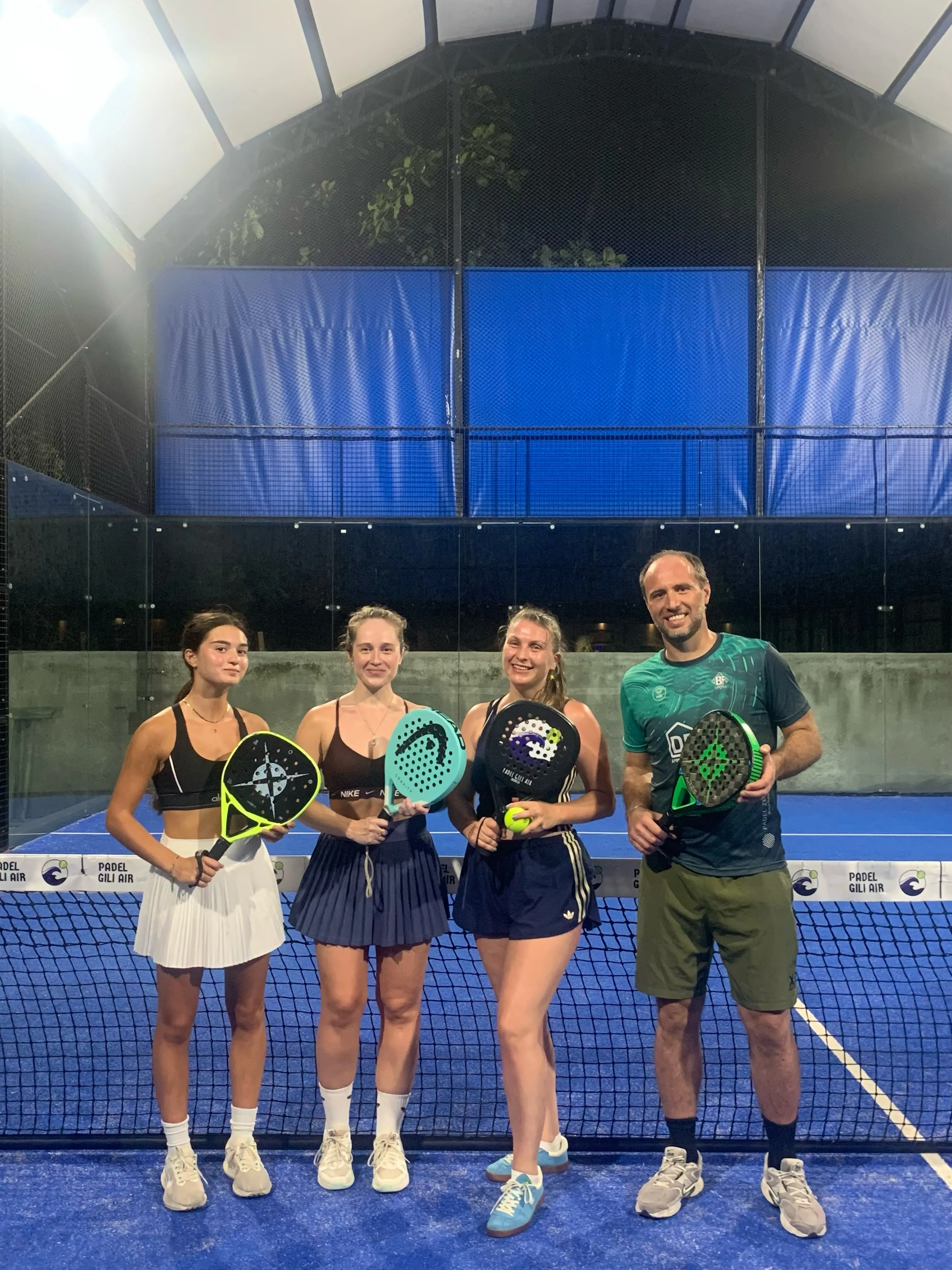 Four padel players holding rackets standing together at the net on a blue court.