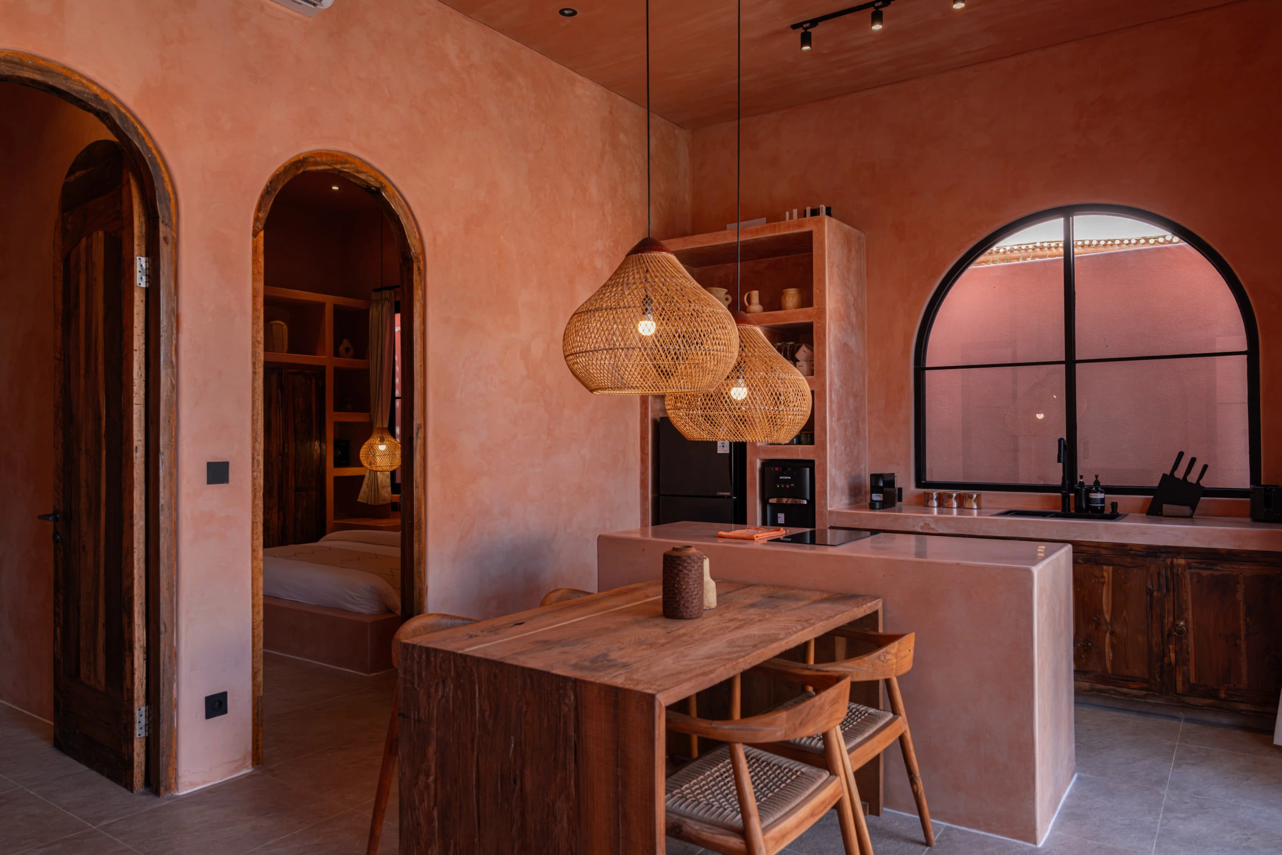 A modern villa kitchen and dining area featuring warm terracotta walls and woven pendant lights.