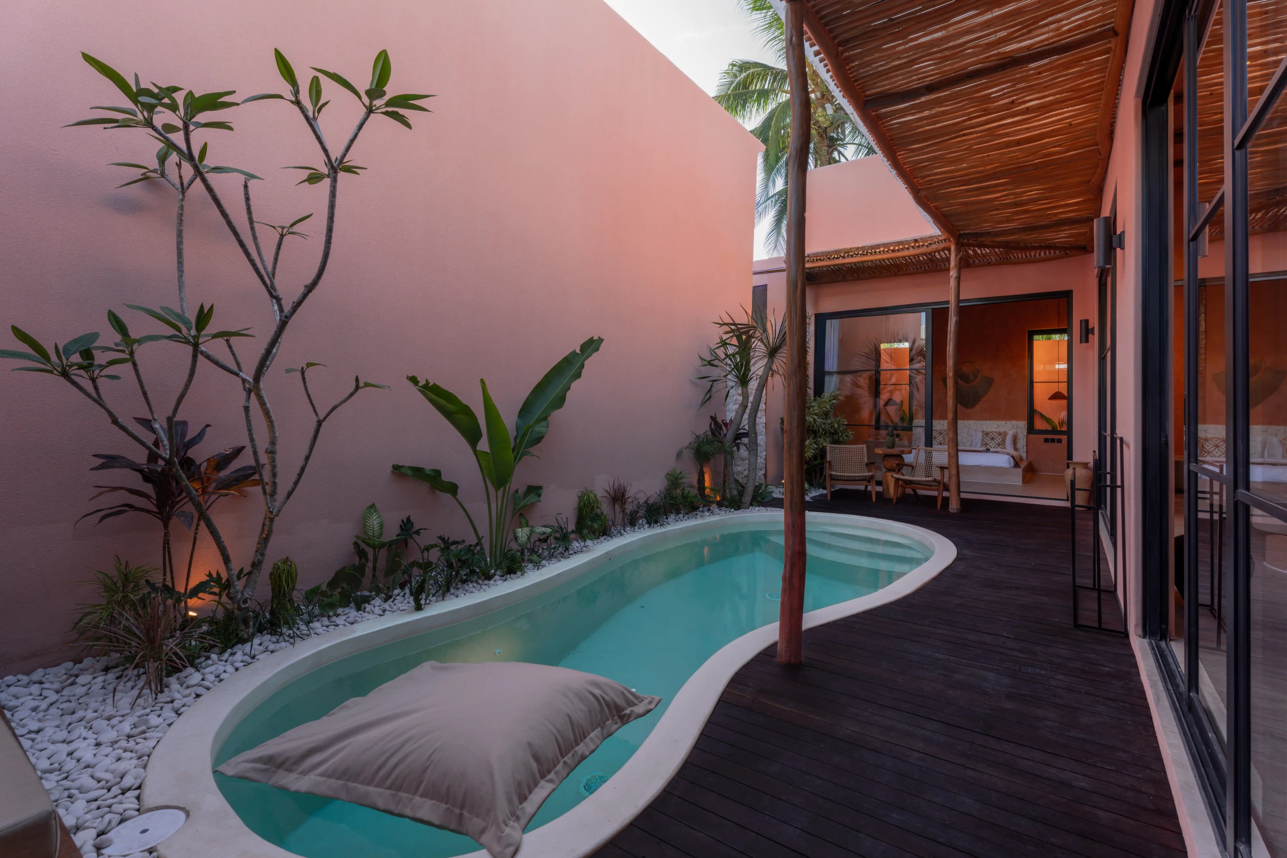 A private villa courtyard featuring a narrow plunge pool, wooden deck, and tropical plants against terracotta walls.