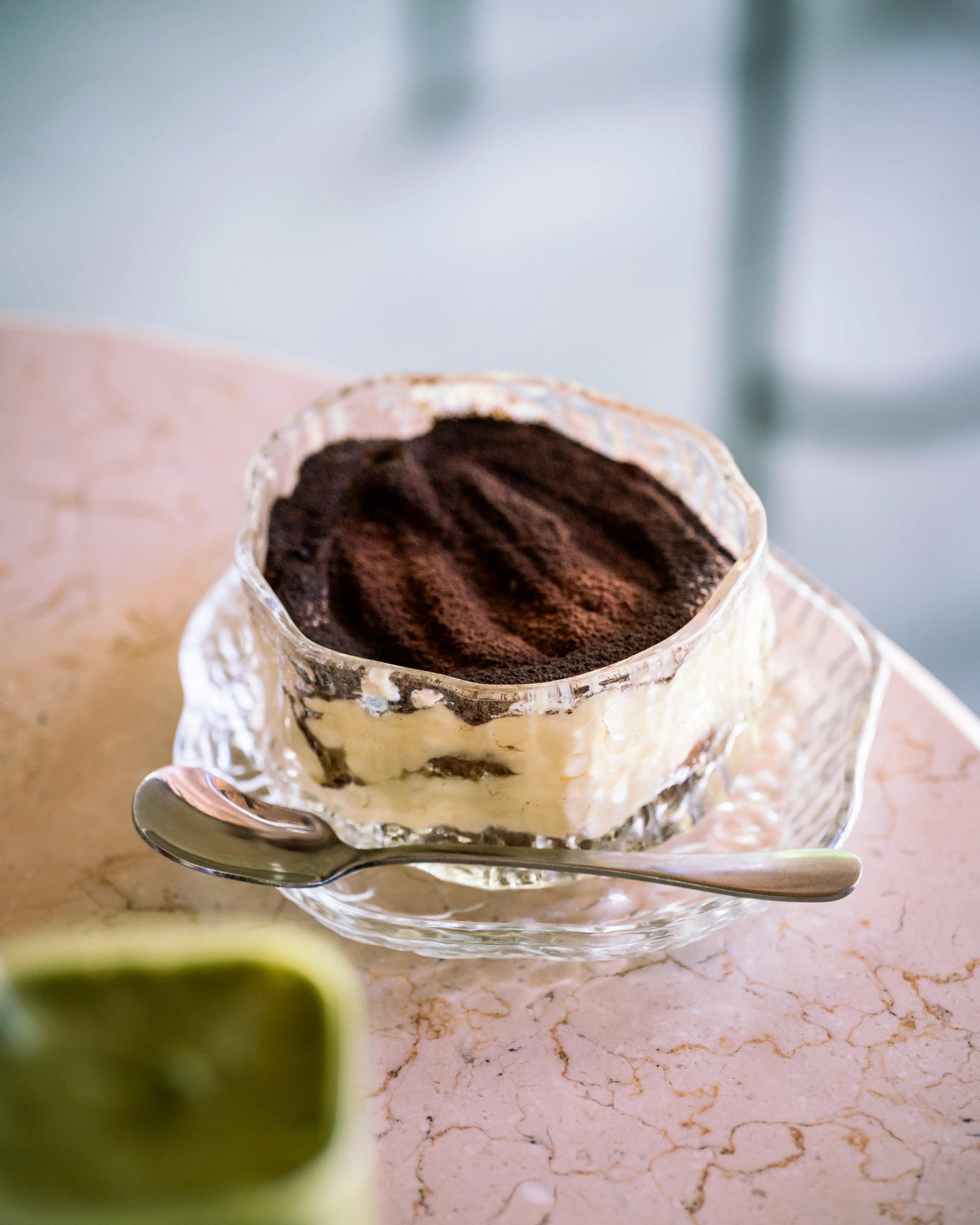 Tiramisu served in a clear glass bowl with a spoon on the side