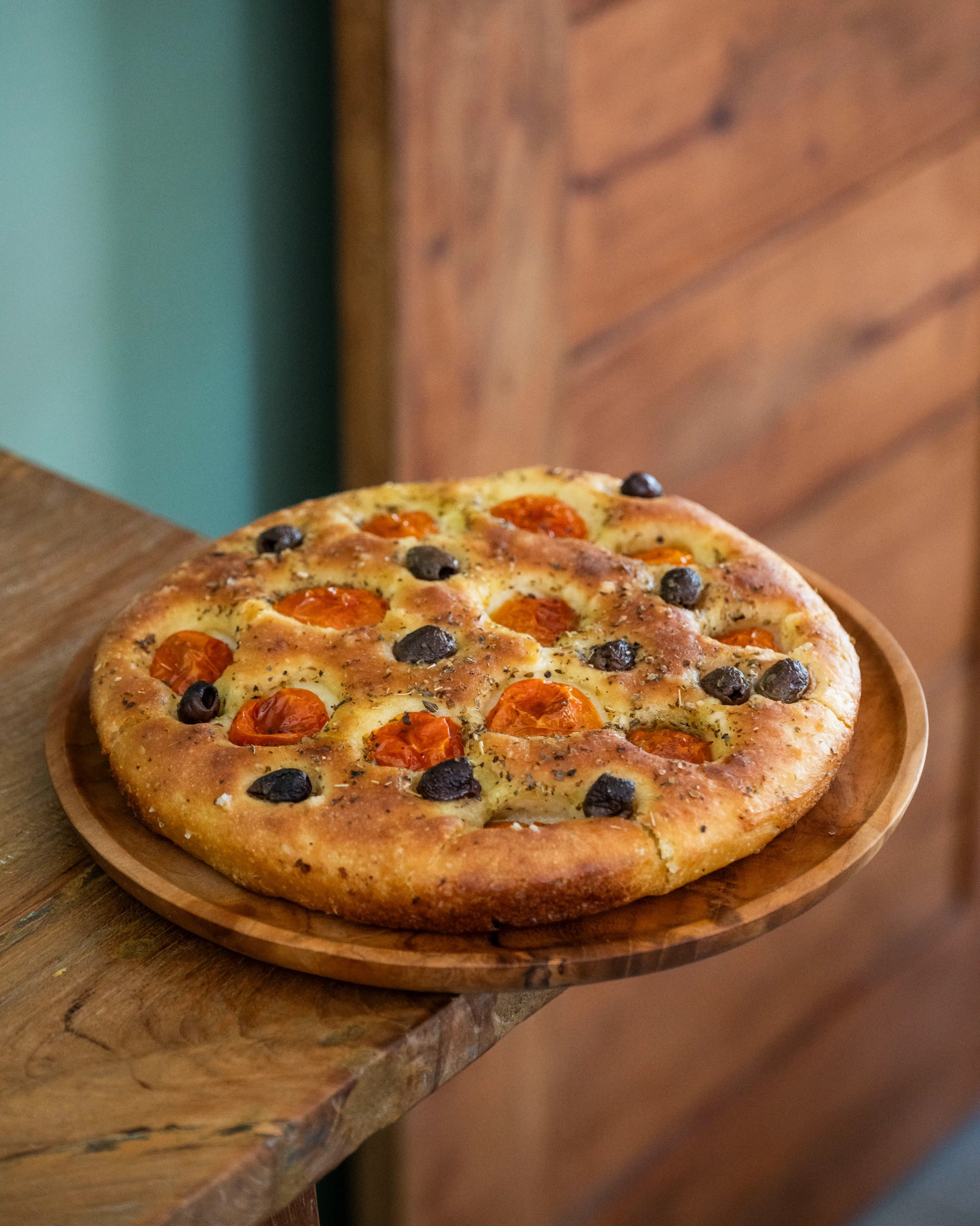 Freshly baked focaccia bread topped with cherry tomatoes and black olives on a wooden plate