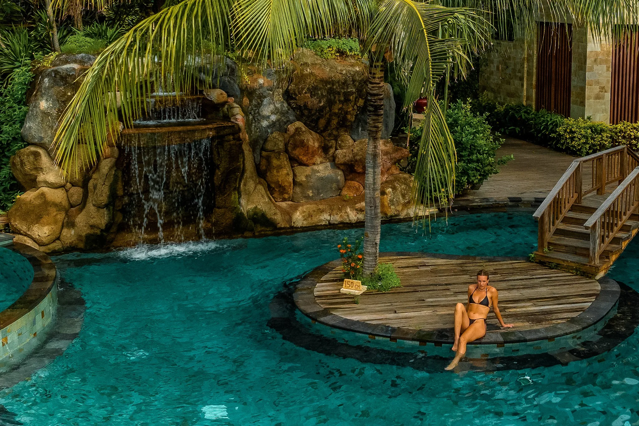 Woman sitting by a pool island with a rocky waterfall.