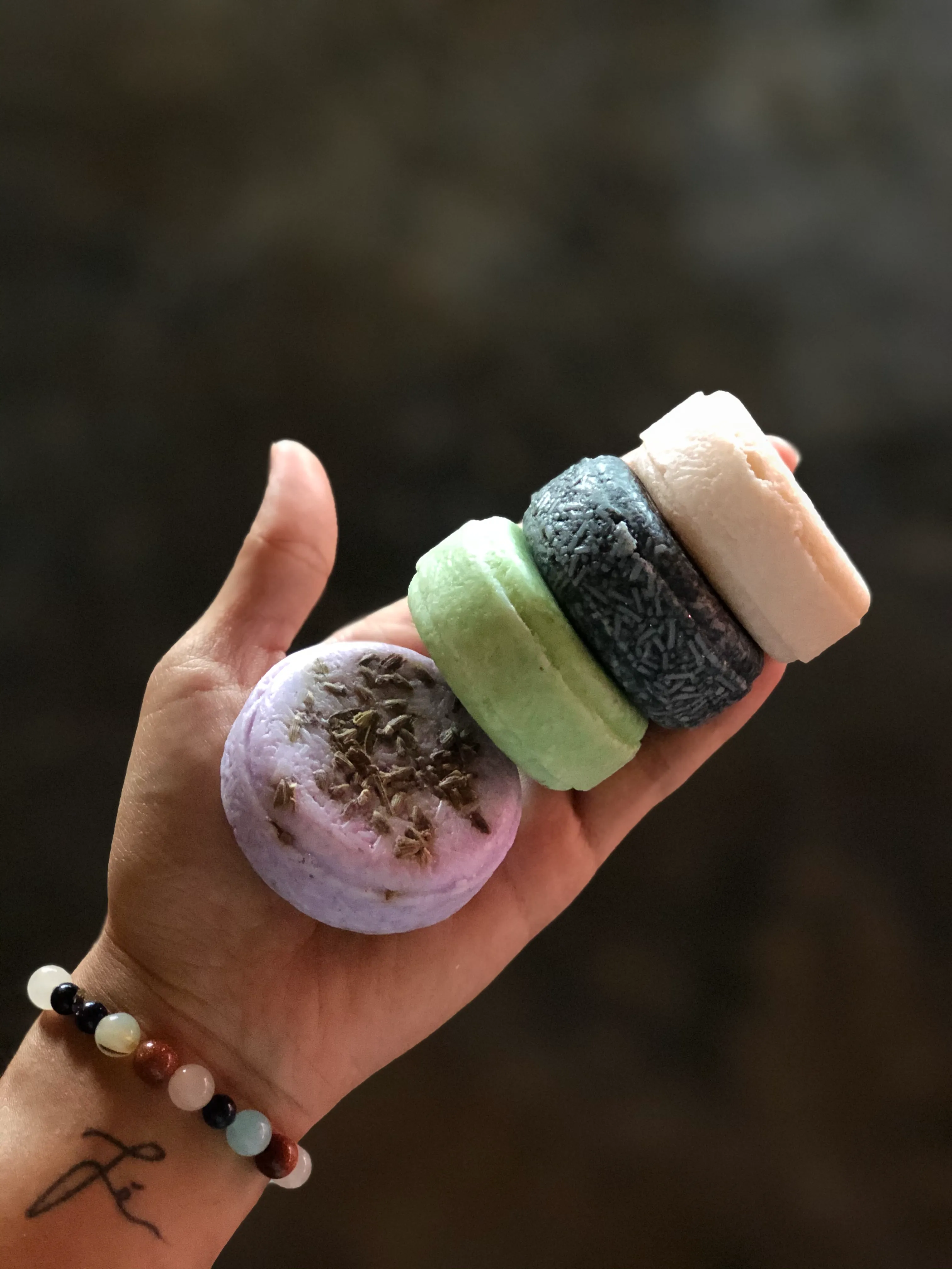 Hand holding four colorful round shampoo bars.